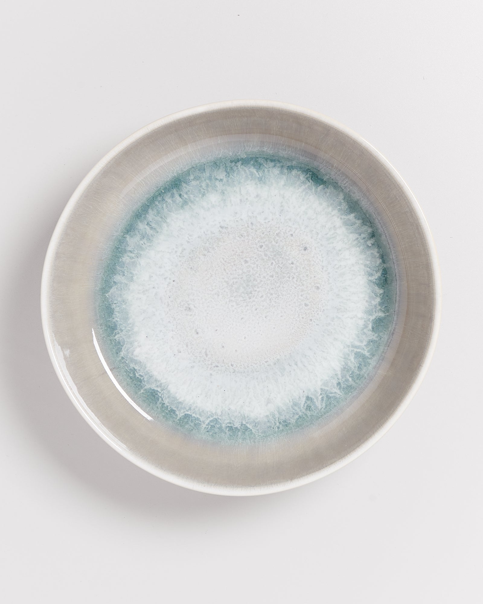 Keramikteller mit blau-weißer Glasur, die einen wasserähnlichen Effekt erzeugt, auf weißem Hintergrund.