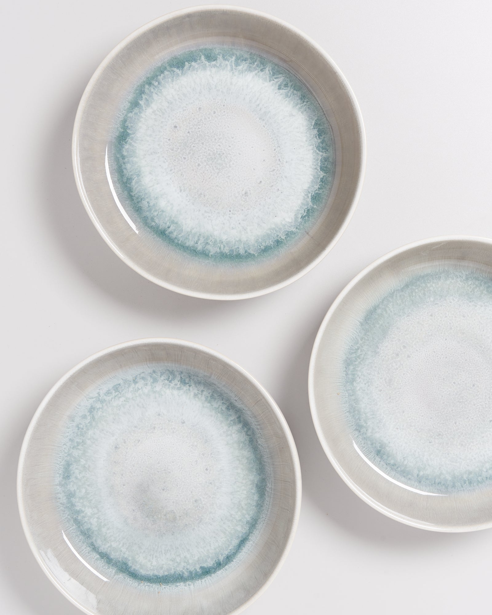 Drei weiße Teller mit blauen, aquarellähnlichen Mustern am Rand auf einer weißen Oberfläche.