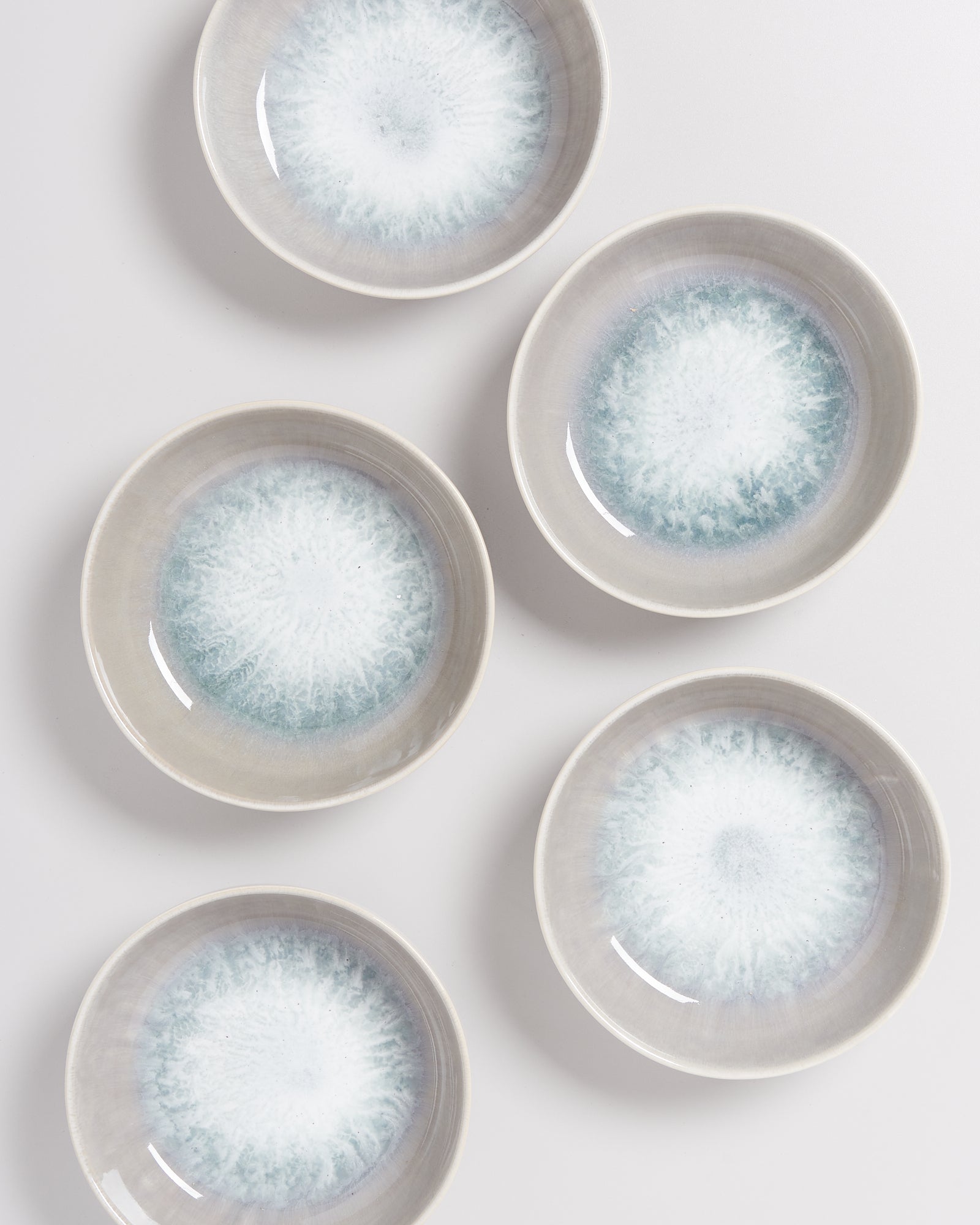 Fünf runde Schalen mit einem grauen Rand und einem spiralförmigen Muster in Blau- und Weißtönen auf weißem Hintergrund.