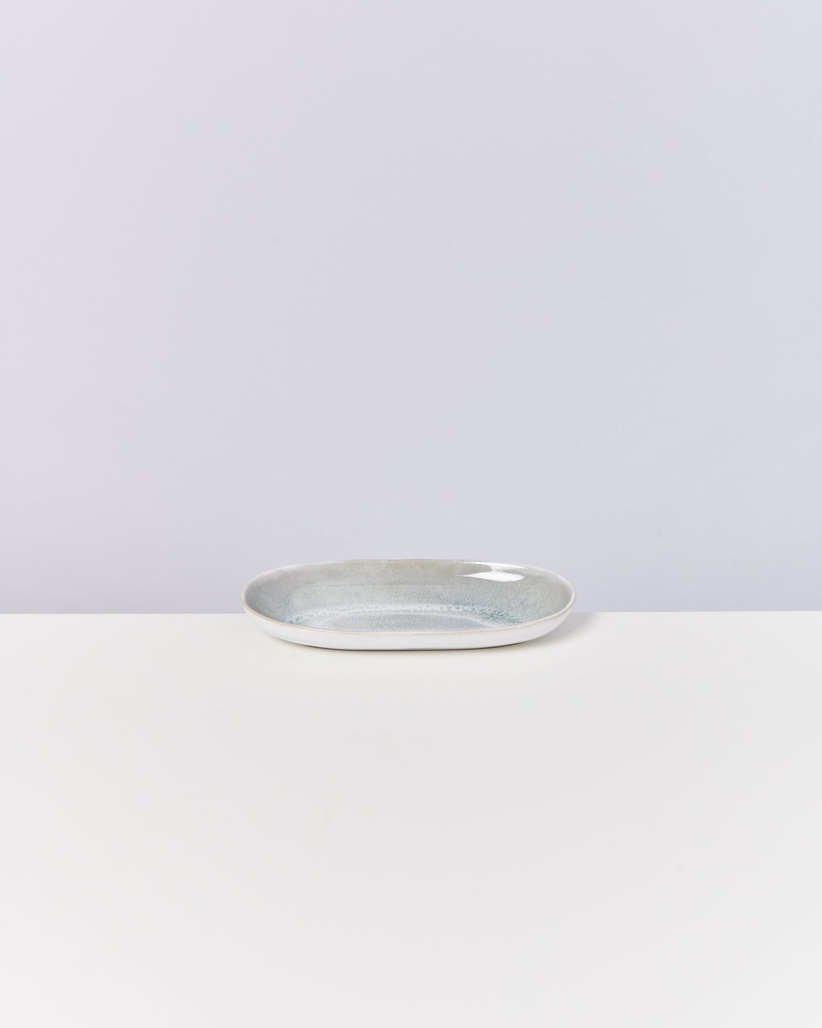 Ovale, graue Keramikschale auf einem weißen Tisch vor einem hellgrauen Hintergrund.