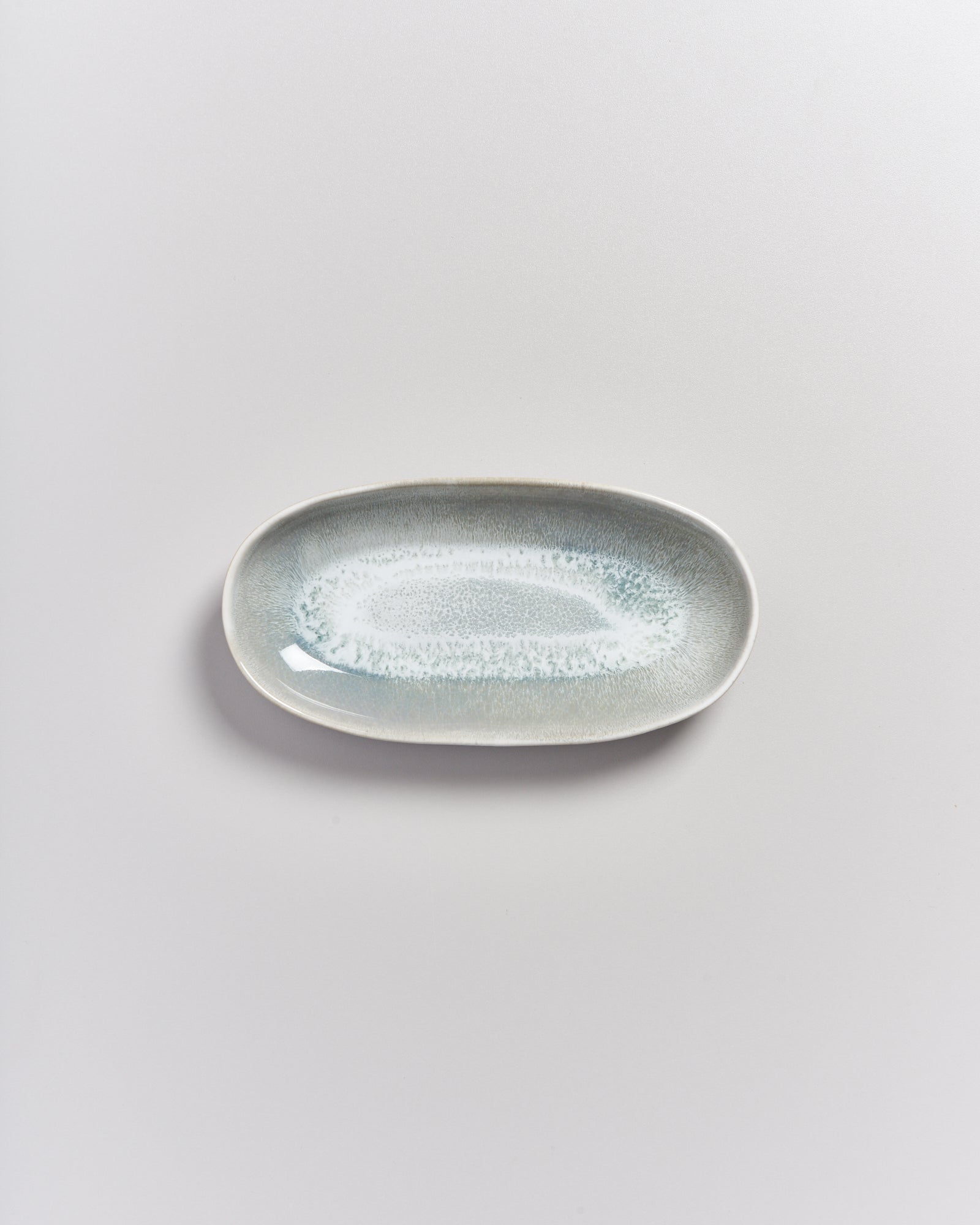 Grauer, ovaler Keramikteller mit hellblauer Glasur auf weißem Hintergrund.