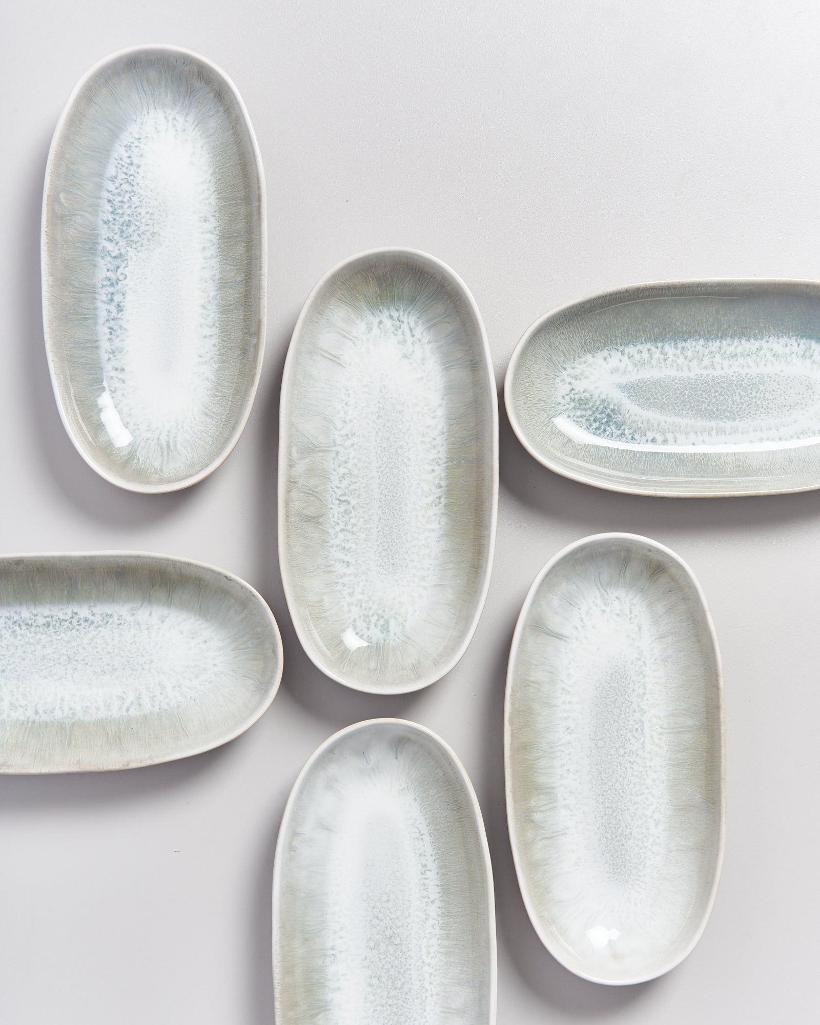 Sechs ovale Keramikteller mit grauem und weißem Muster liegen auf einem weißen Untergrund.