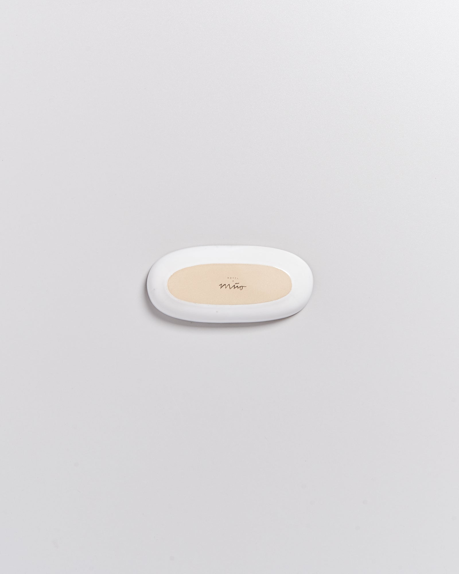 Ein ovales, weißes Plastikobjekt mit einem beigefarbenen Einsatz und dem Schriftzug "Miro" darauf, auf grauem Hintergrund.