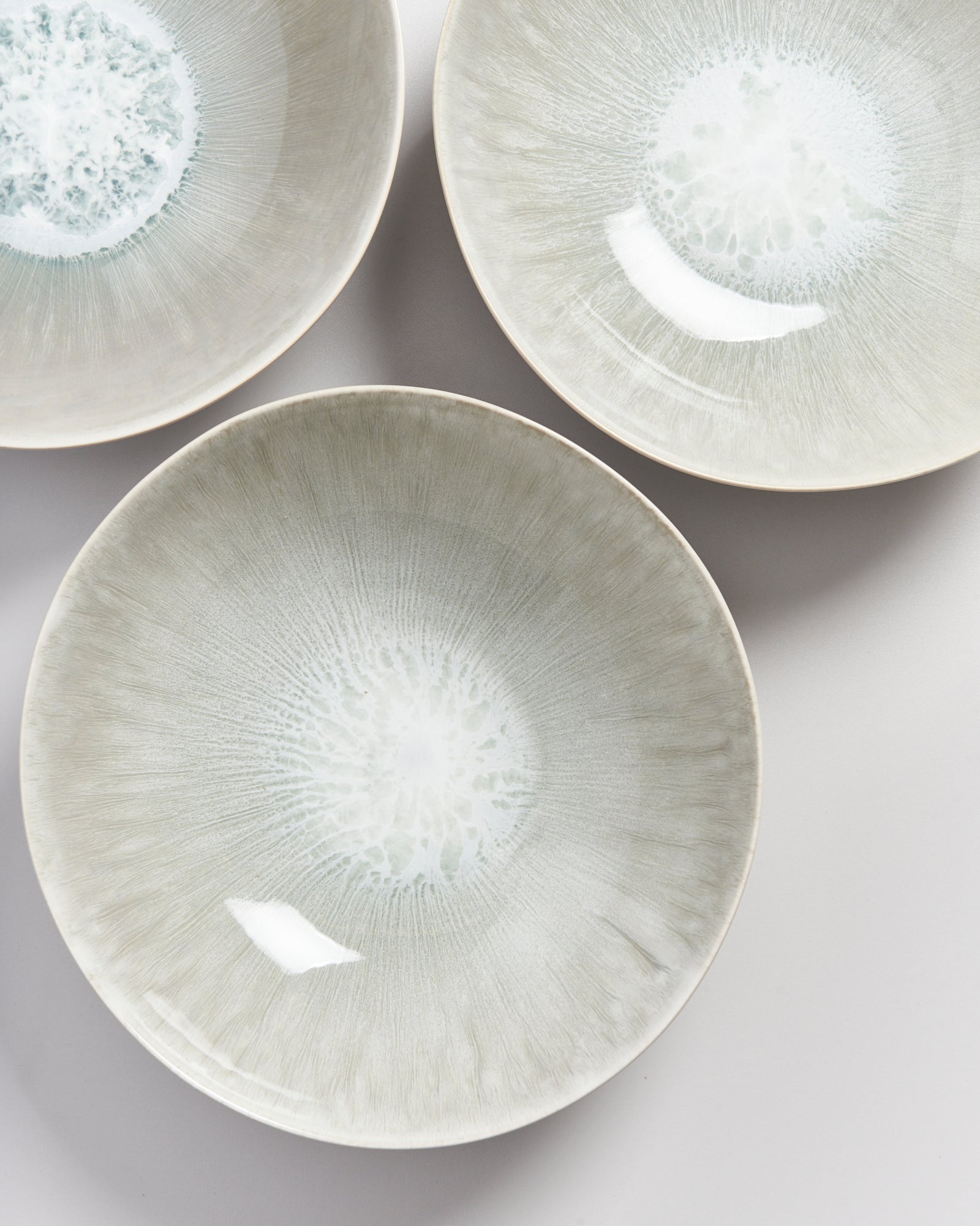 Drei beige Schalen mit weißem, radialen Muster und glänzender Oberfläche auf hellem Hintergrund.