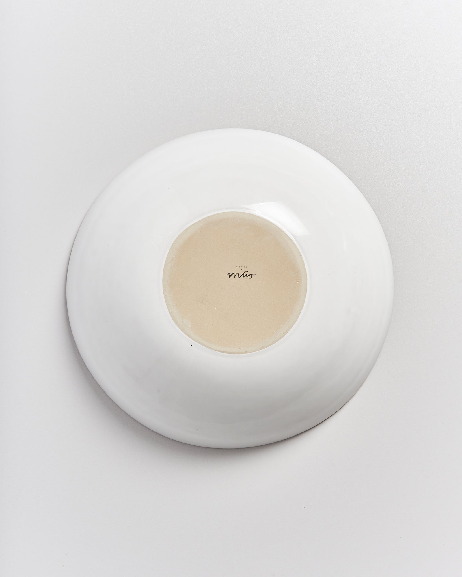 Eine umgedrehte weiße Schüssel mit hellbraunem Boden und Beschriftung darauf, auf einer weißen Oberfläche.