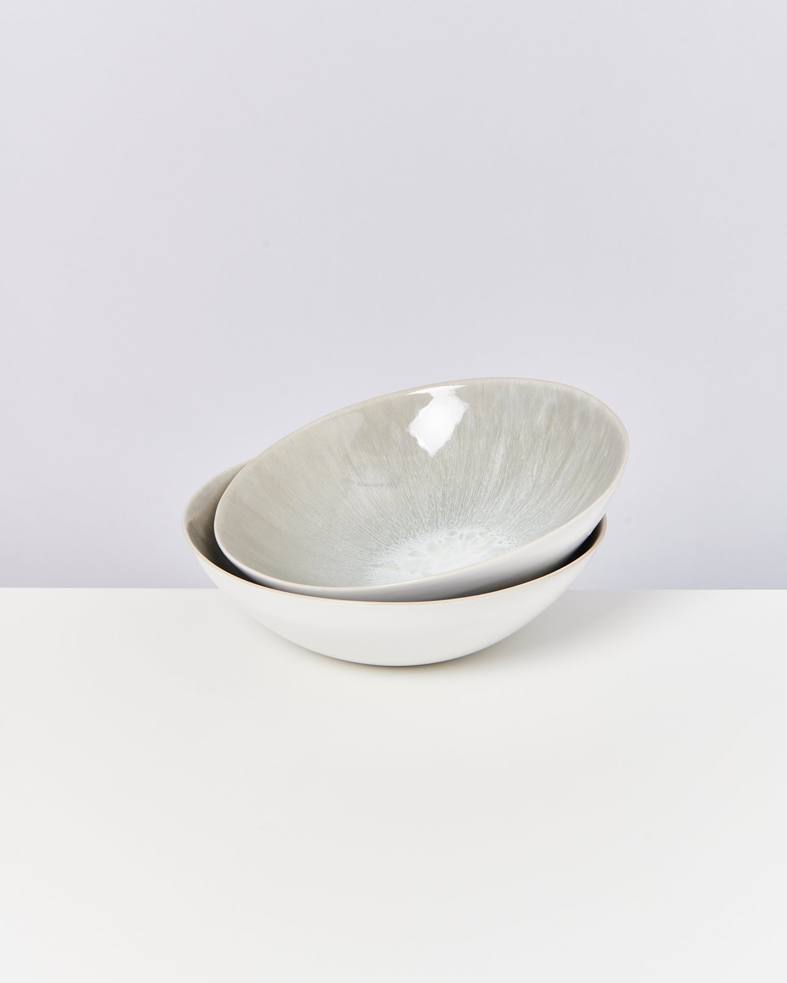 Zwei ineinander gestapelte, weiß-graue Keramikschalen auf einer weißen Oberfläche.