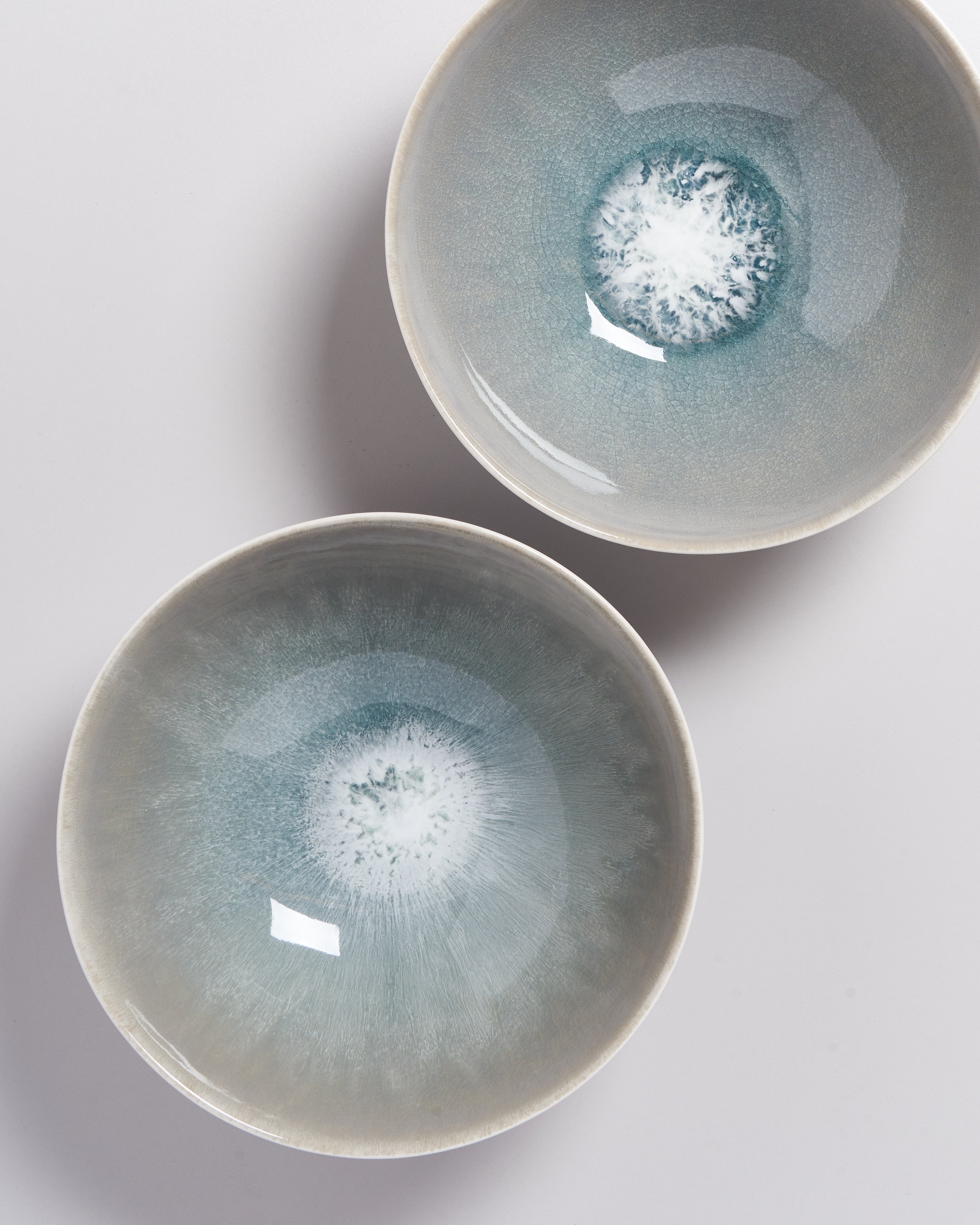 Zwei Keramikschalen mit bläulicher, kristallartiger Glasur auf weißem Hintergrund von oben.