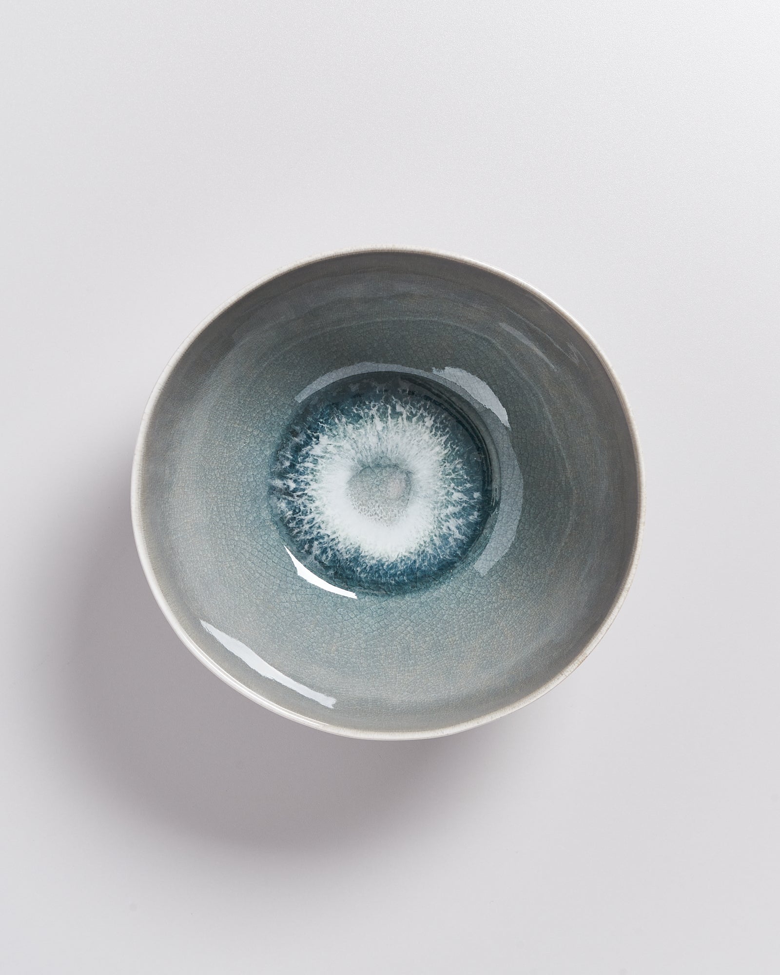 Keramikschale mit blau-weißer Glasur, die an einen Wasserwirbel erinnert, auf weißem Hintergrund.