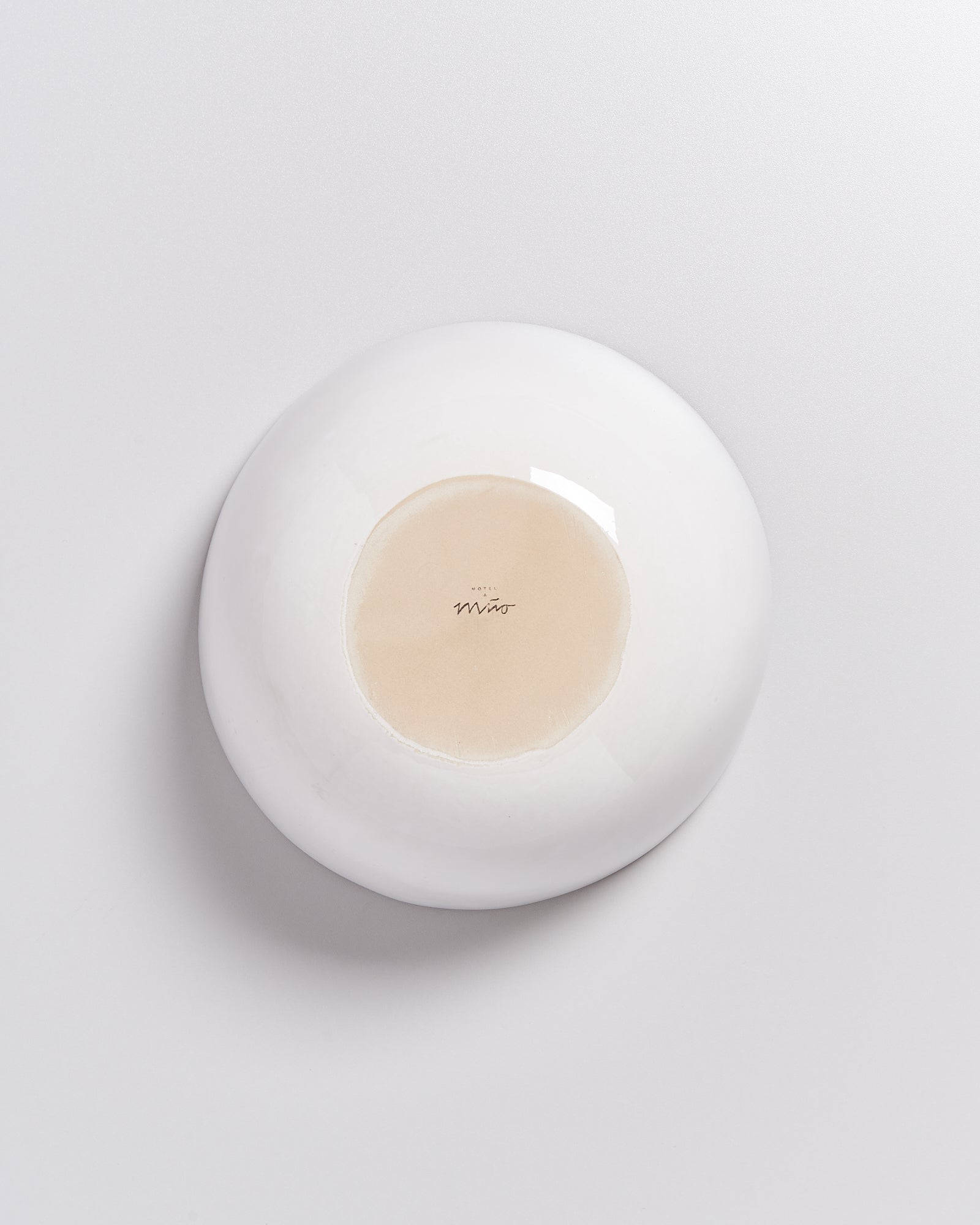 Eine umgedrehte, runde, weiße Schale mit einem beigen Boden und einem kleinen Logo in der Mitte.