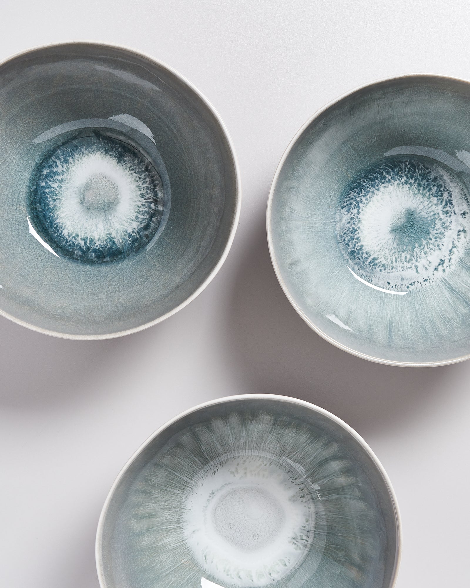 Drei kunstvoll glasierte, runde Schalen mit graublauen, kreisförmigen Mustern auf hellem Hintergrund.