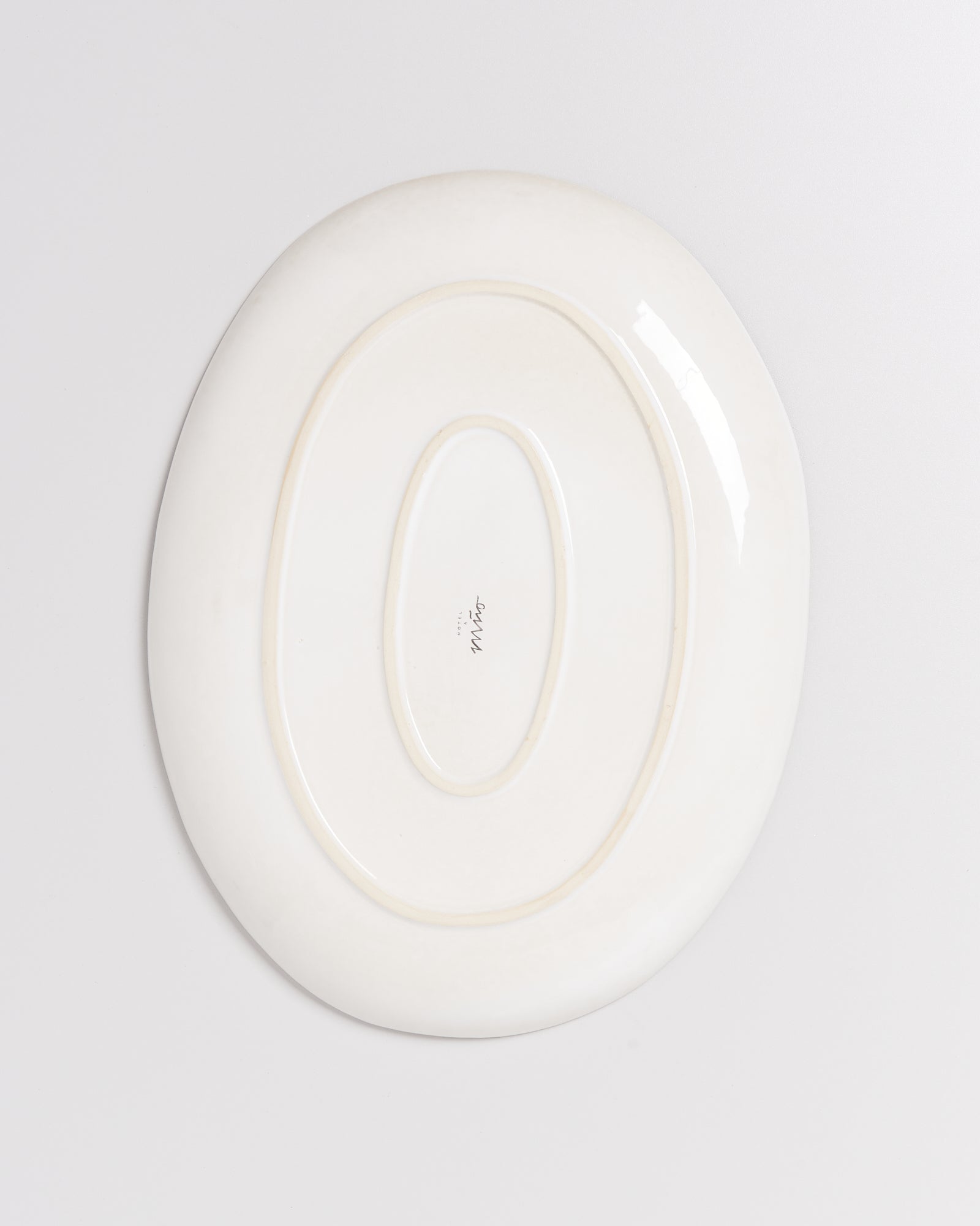 Rückseite eines ovalen, weißen Keramiktellers mit einer ovalen Vertiefung in der Mitte und einem Schriftzug darauf.