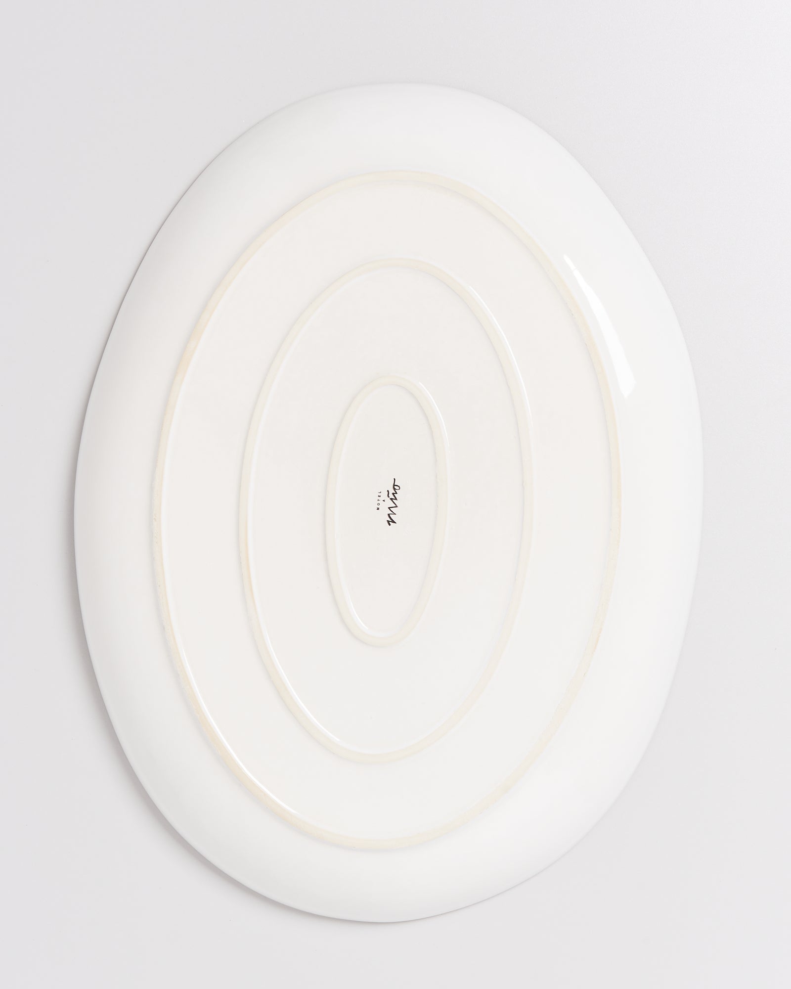 Weiße ovale Platte mit konzentrischen Rillen und aufgedrucktem Text in der Mitte auf einer hellgrauen Oberfläche.