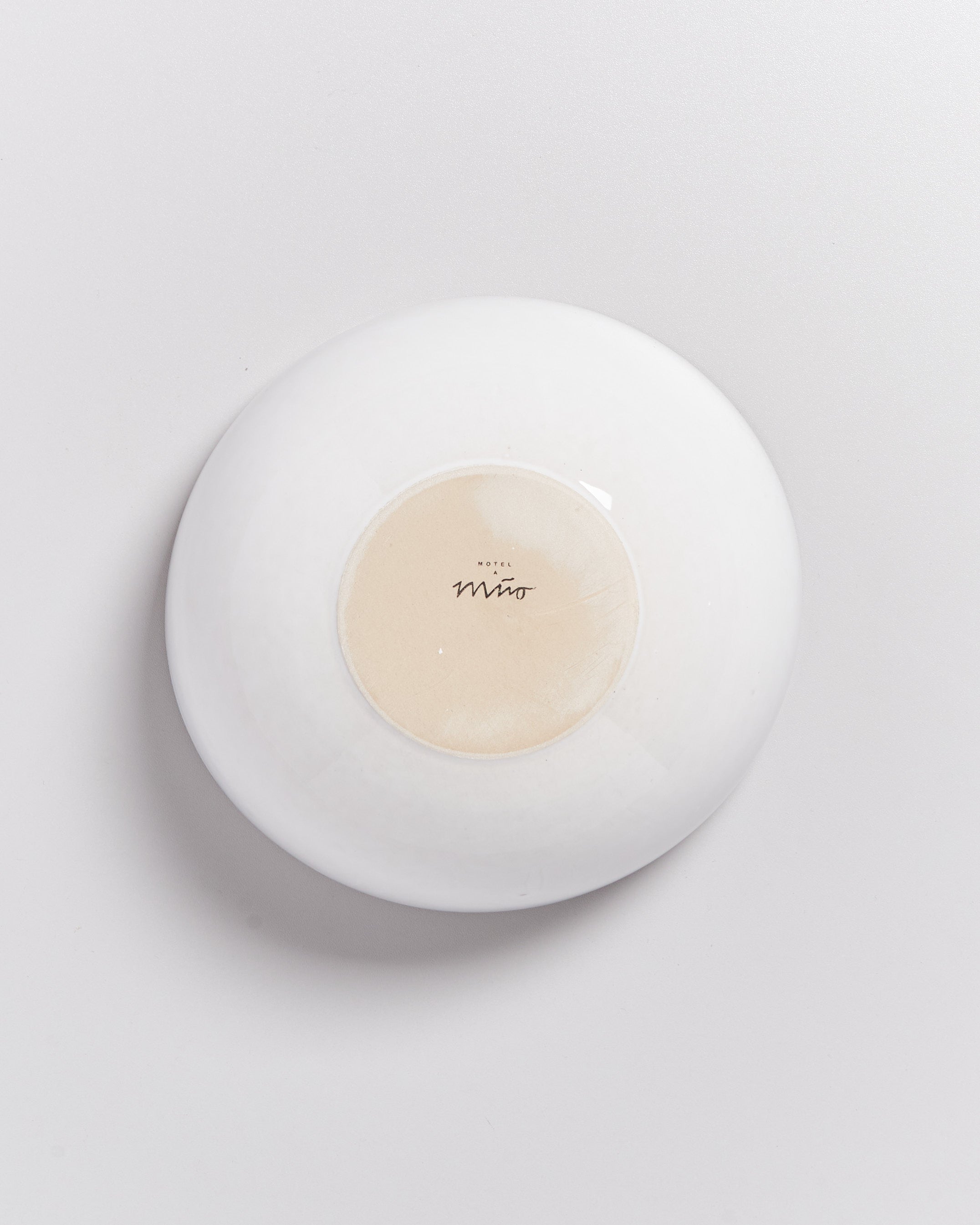 Runde, umgedrehte weiße Schale auf hellem Hintergrund mit Aufschrift "Hotel Miro" auf der Unterseite.
