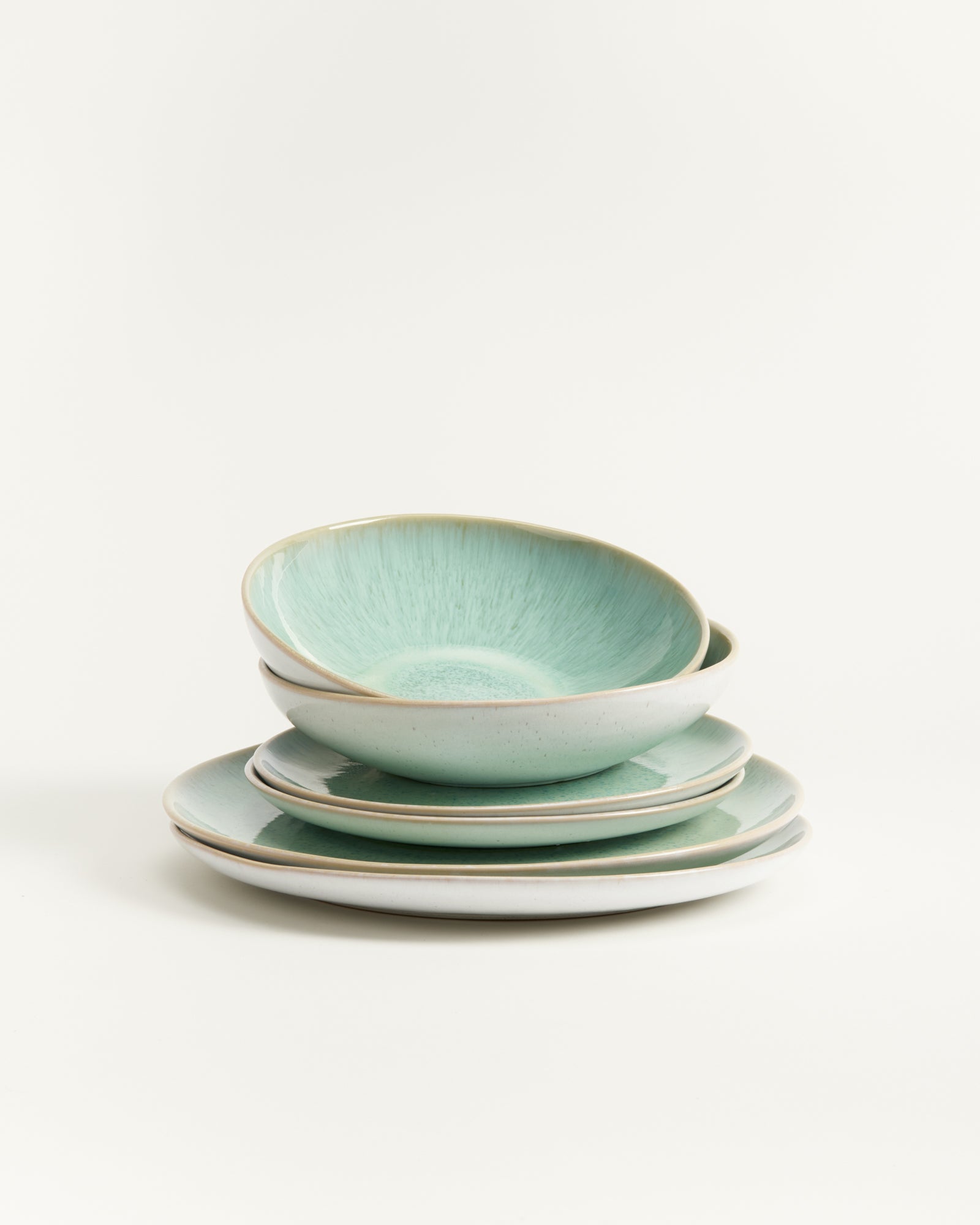 Ein Stapel aus zwei blauen Schalen und zwei Tellern mit beigem Rand auf einem weißen Hintergrund.