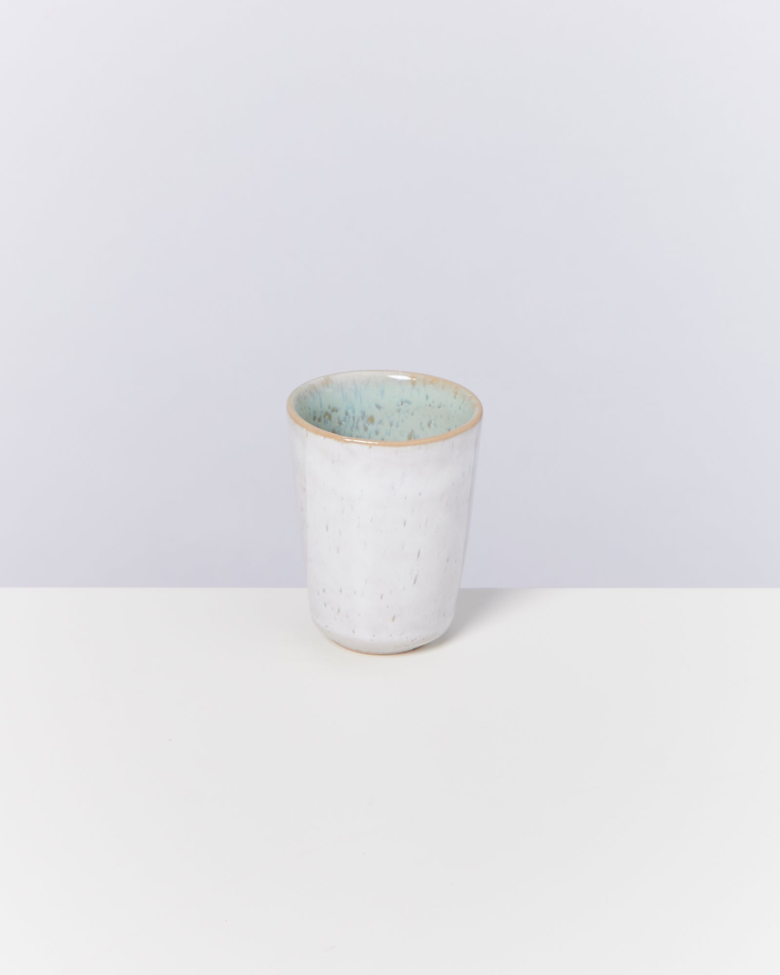 Weißer Keramikbecher mit hellblauer Glasur innen, auf weißem Hintergrund.