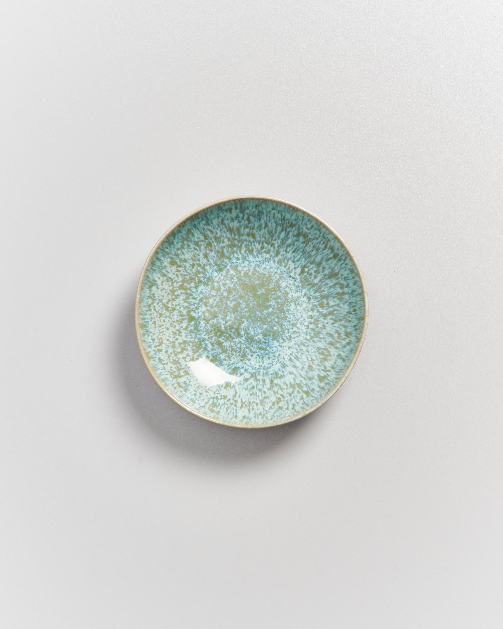 Kleiner Teller mit blauer und grüner Sprenkelmusterung auf weißem Hintergrund.