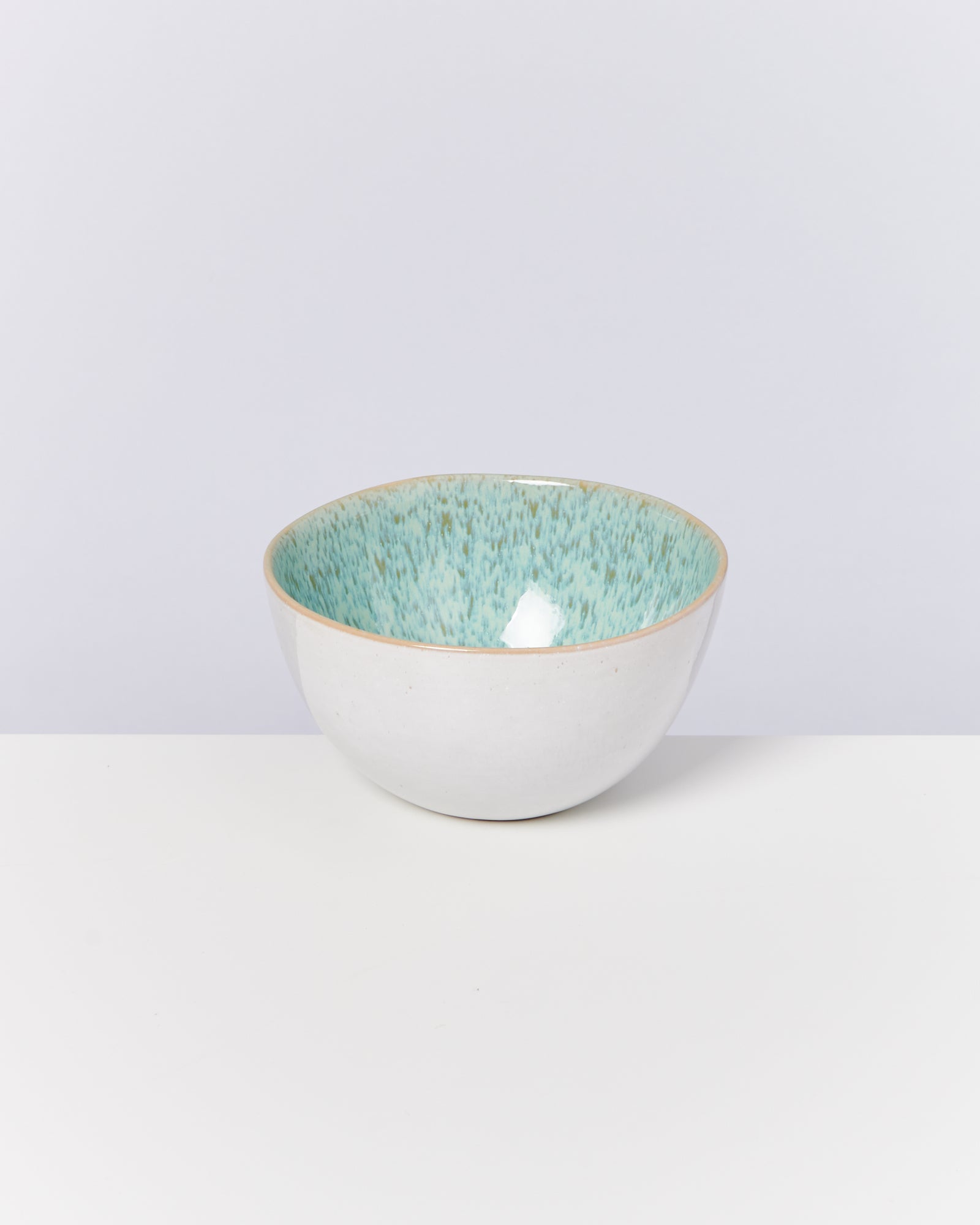 Weiße Keramikschüssel mit türkisfarbener Innenseite, auf weißem Hintergrund.