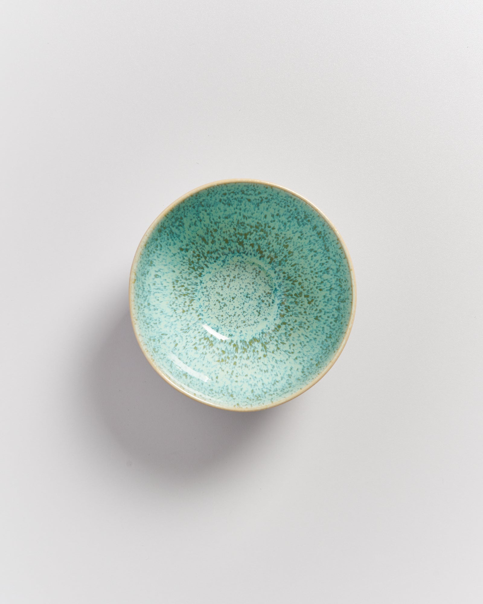 Eine türkisfarbene, gesprenkelte Schale auf einer weißen Oberfläche.