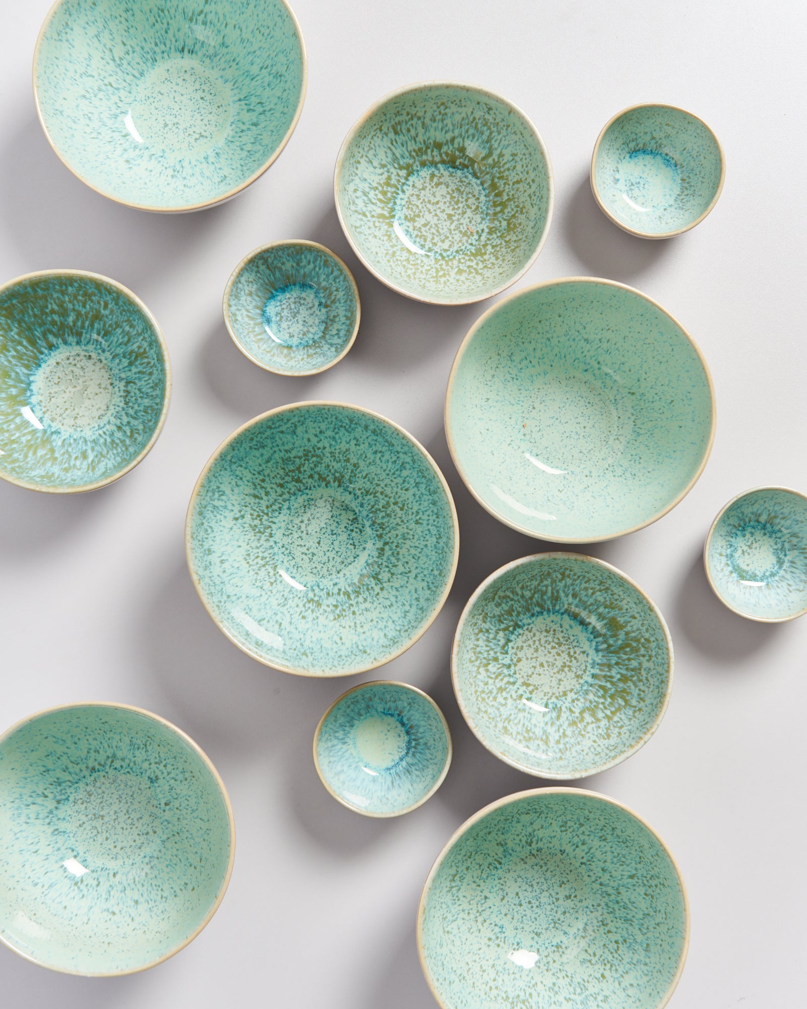 Elfenbeinfarbene Schalen mit türkisgrünem Sprenkelmuster in verschiedenen Größen auf einer hellen Oberfläche.