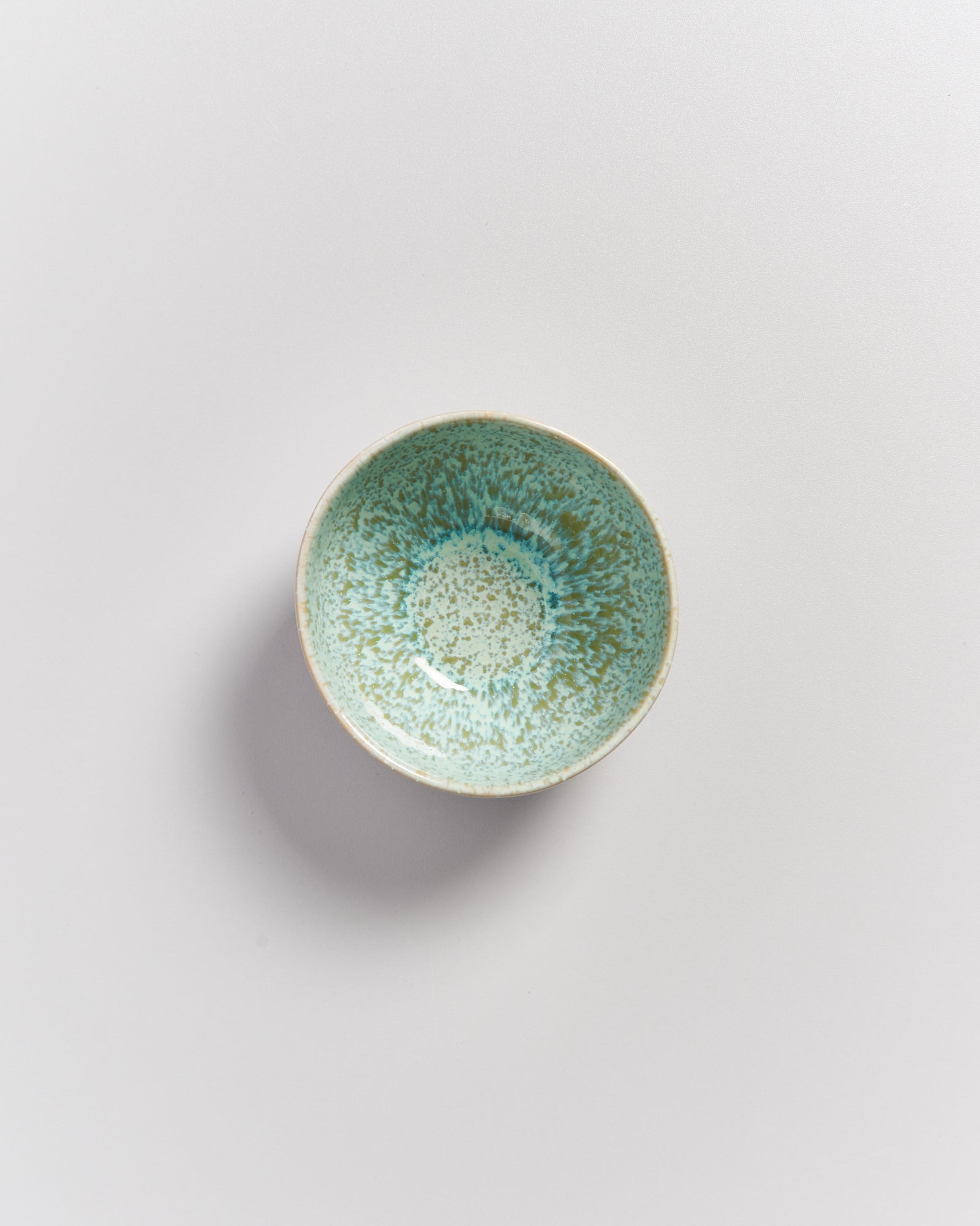 Kleine Schale mit türkis-melierter Glasur auf weißem Hintergrund.