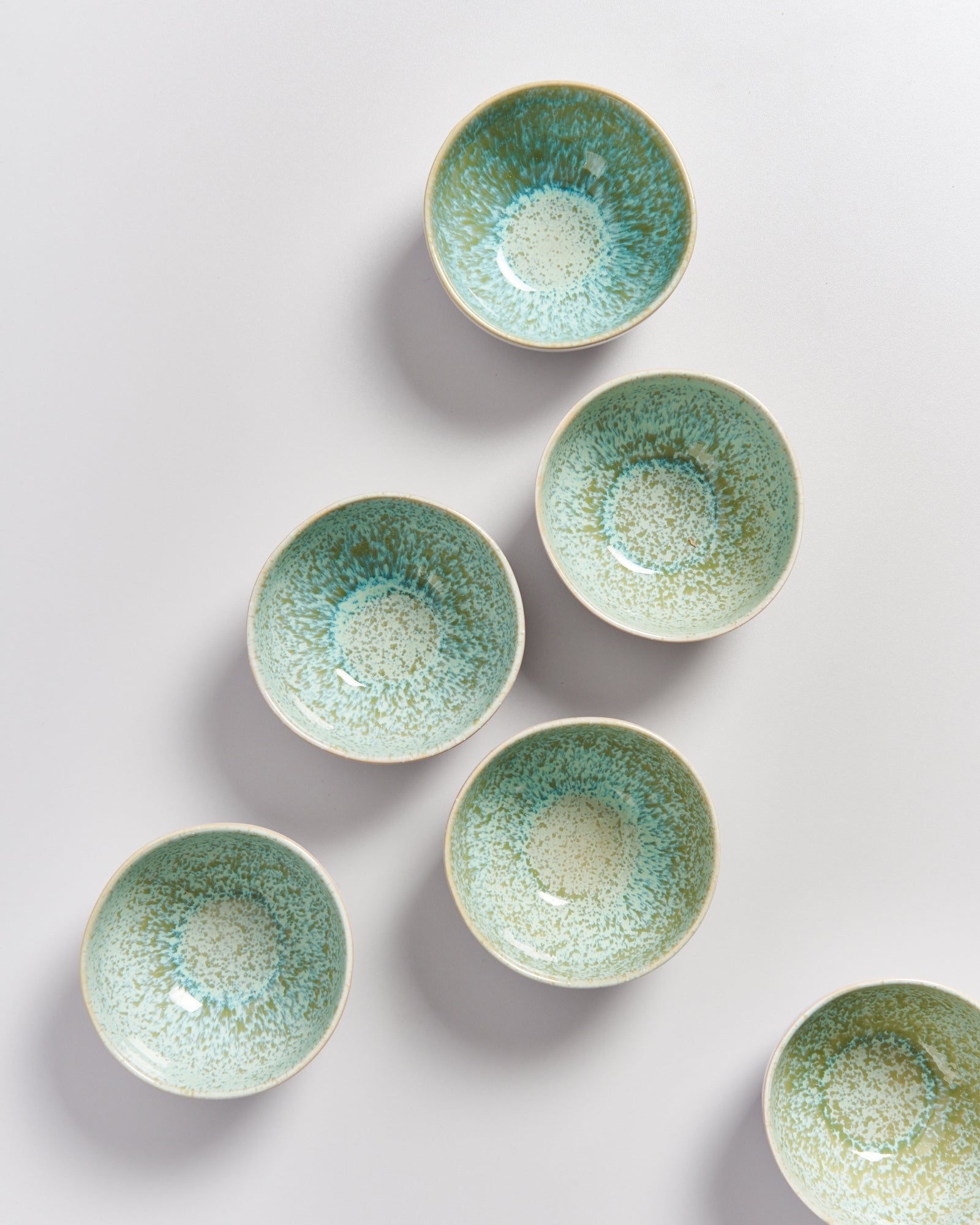 Sechs grün gesprenkelte Schüsseln auf einem weißen Hintergrund, angeordnet in einer Art Diagonale.