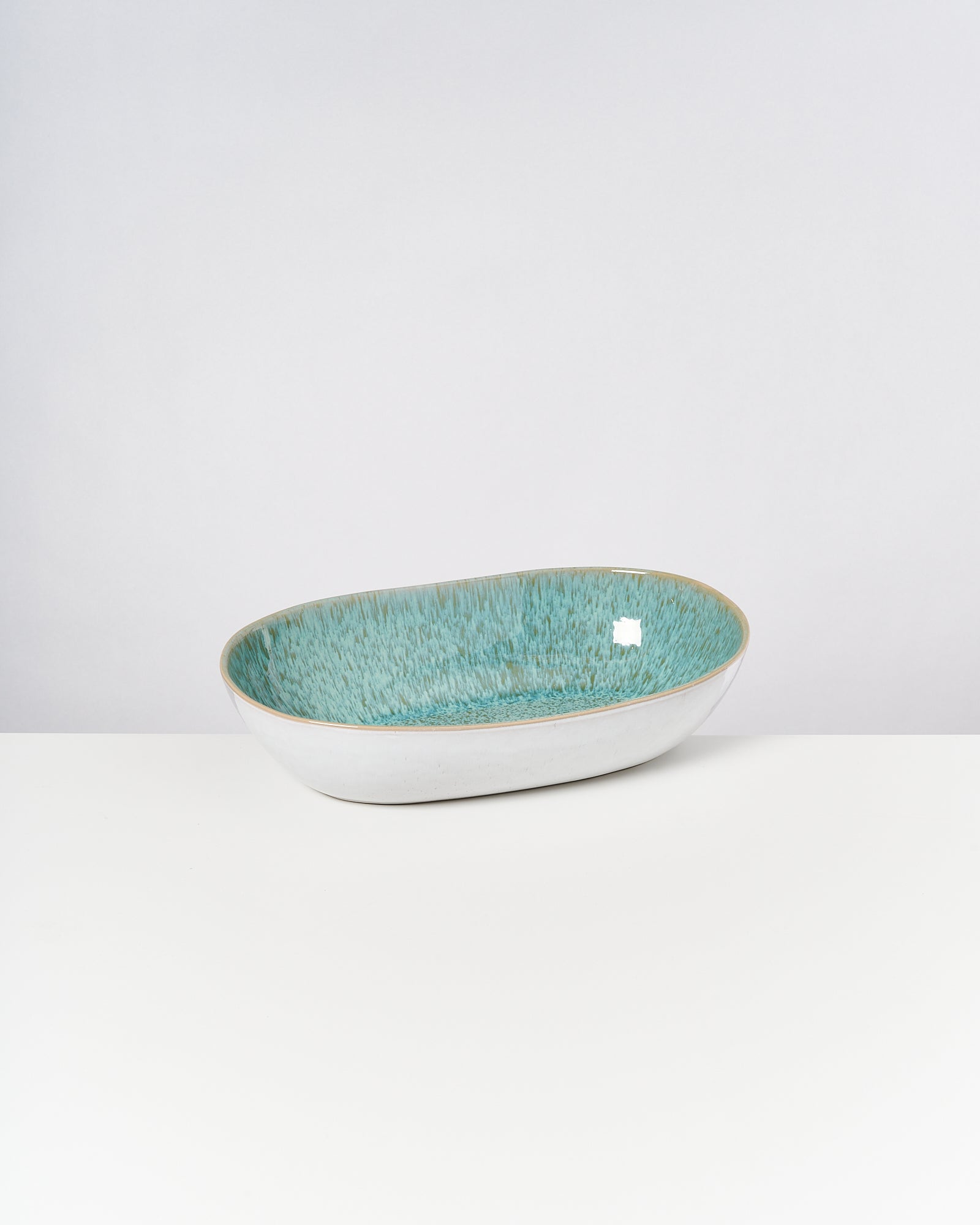 Keramikschale mit türkisfarbener, strukturiert glänzender Innenseite und weißem Rand auf einem weißen Hintergrund.