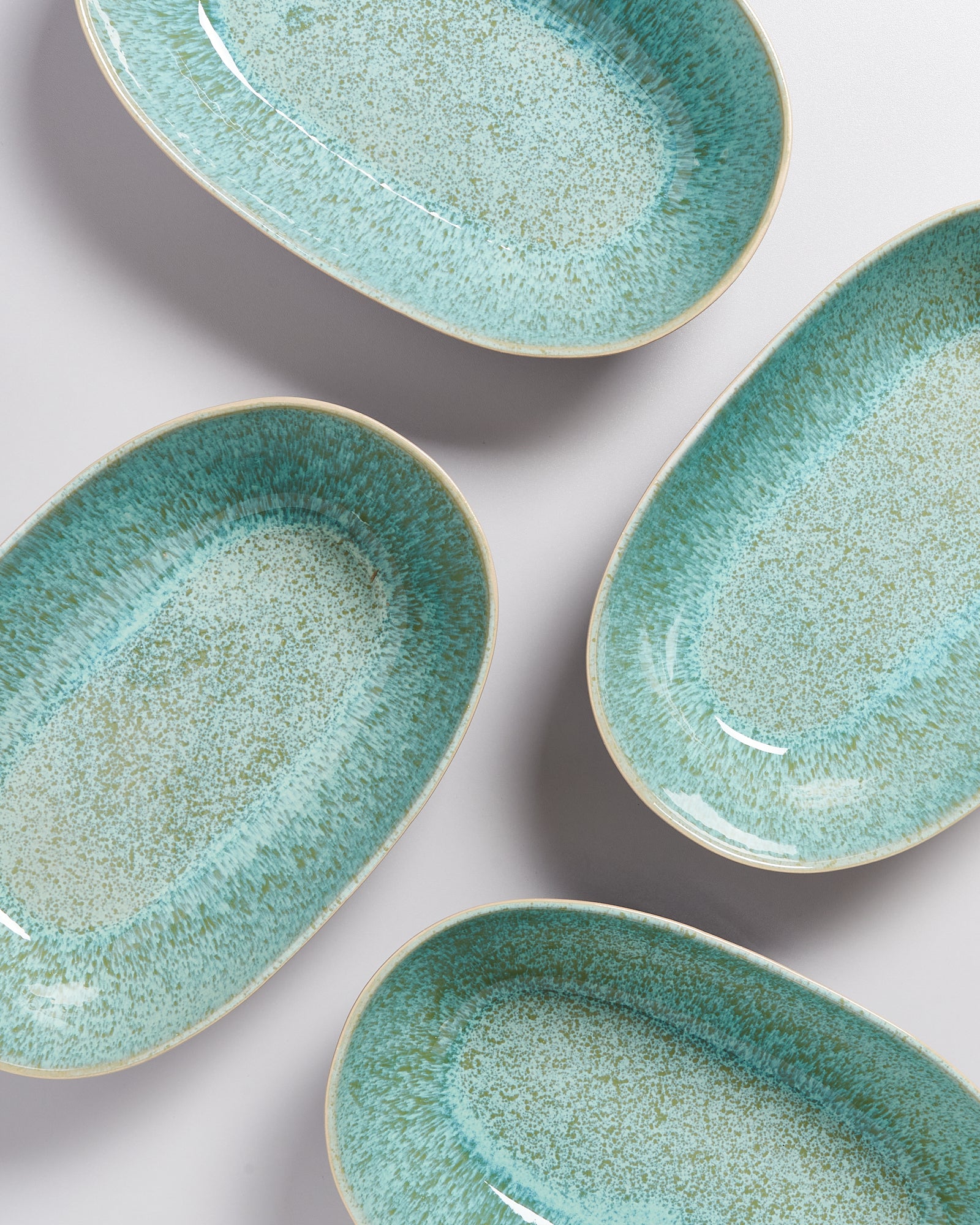 Vier ovale, hellblaue Keramikteller mit gesprenkeltem Muster auf einem hellen Hintergrund angeordnet.