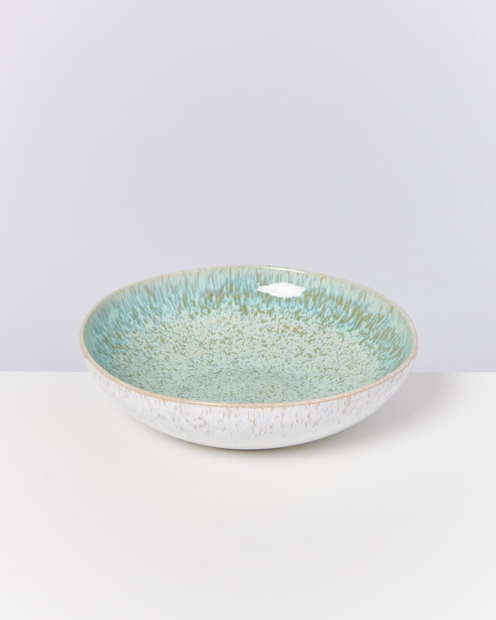 Keramikschüssel mit blau-grüner, gesprenkelter Glasur auf weißem Hintergrund.