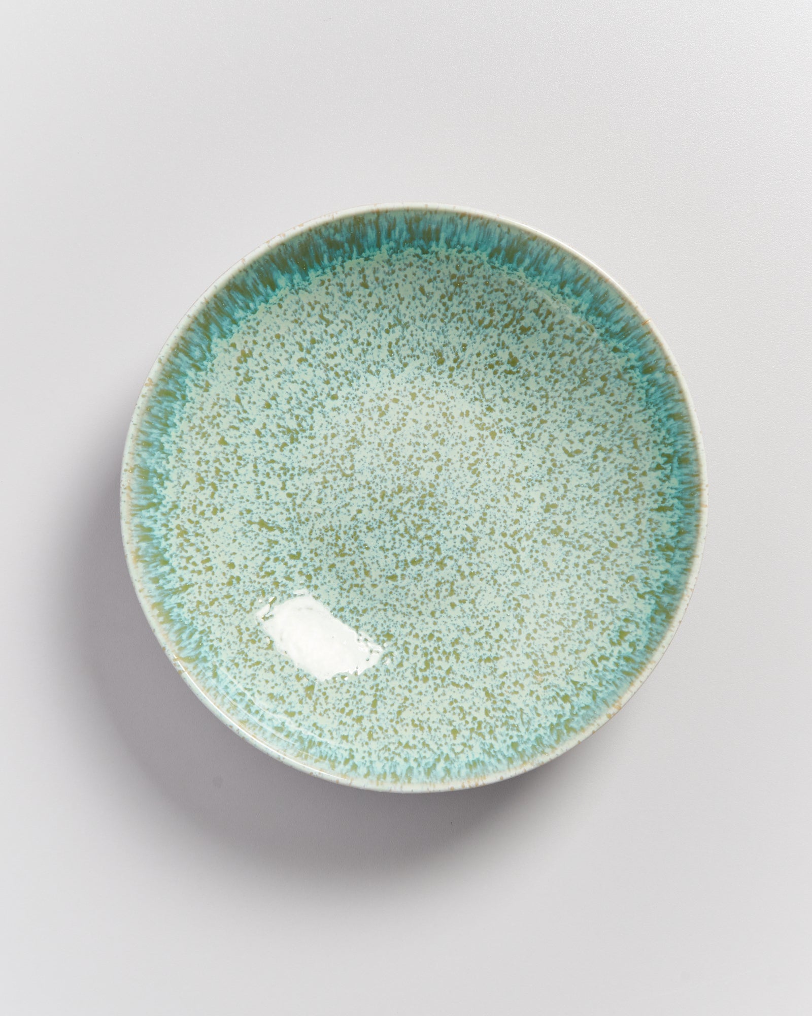 Keramikteller mit grün-blauem Muster auf weißem Hintergrund.