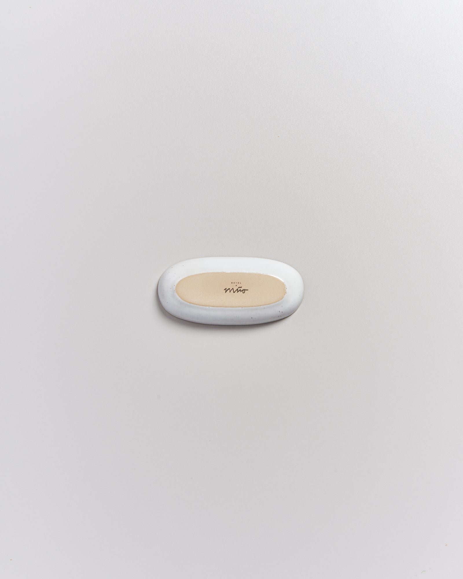 Ein graues ovales Objekt mit cremefarbener Mitte und Aufschrift "Mao" liegt auf einer weißen Oberfläche.