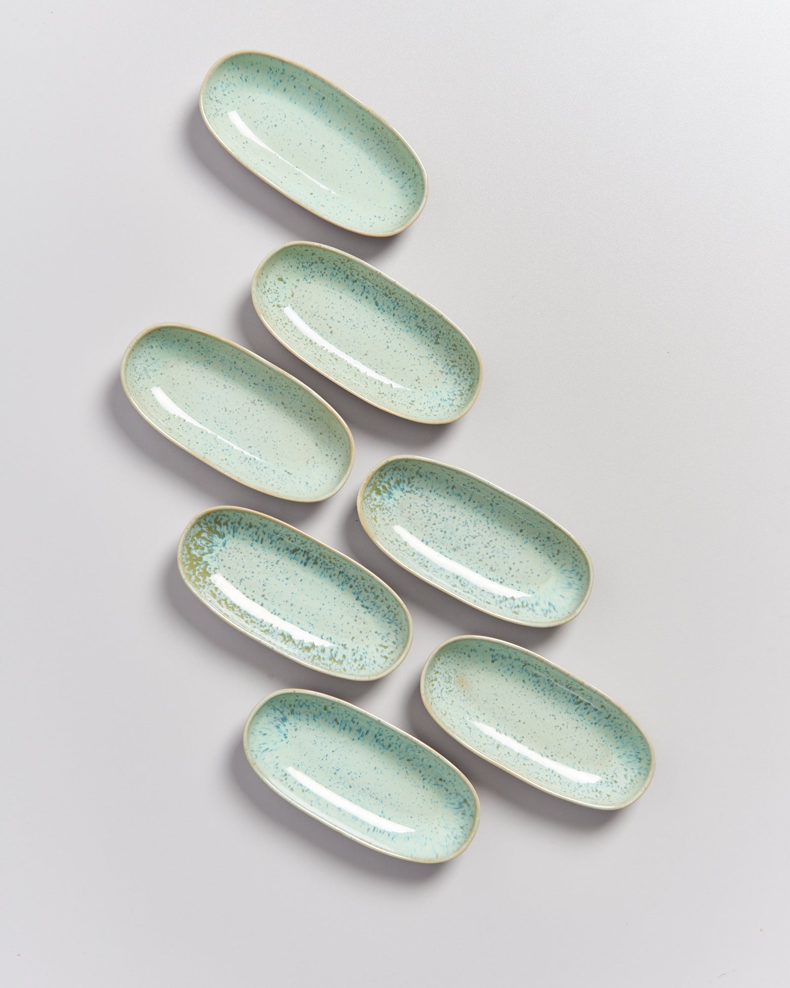 Sieben längliche, pastellgrüne Teller mit Sprenkeln auf einem weißen Hintergrund.