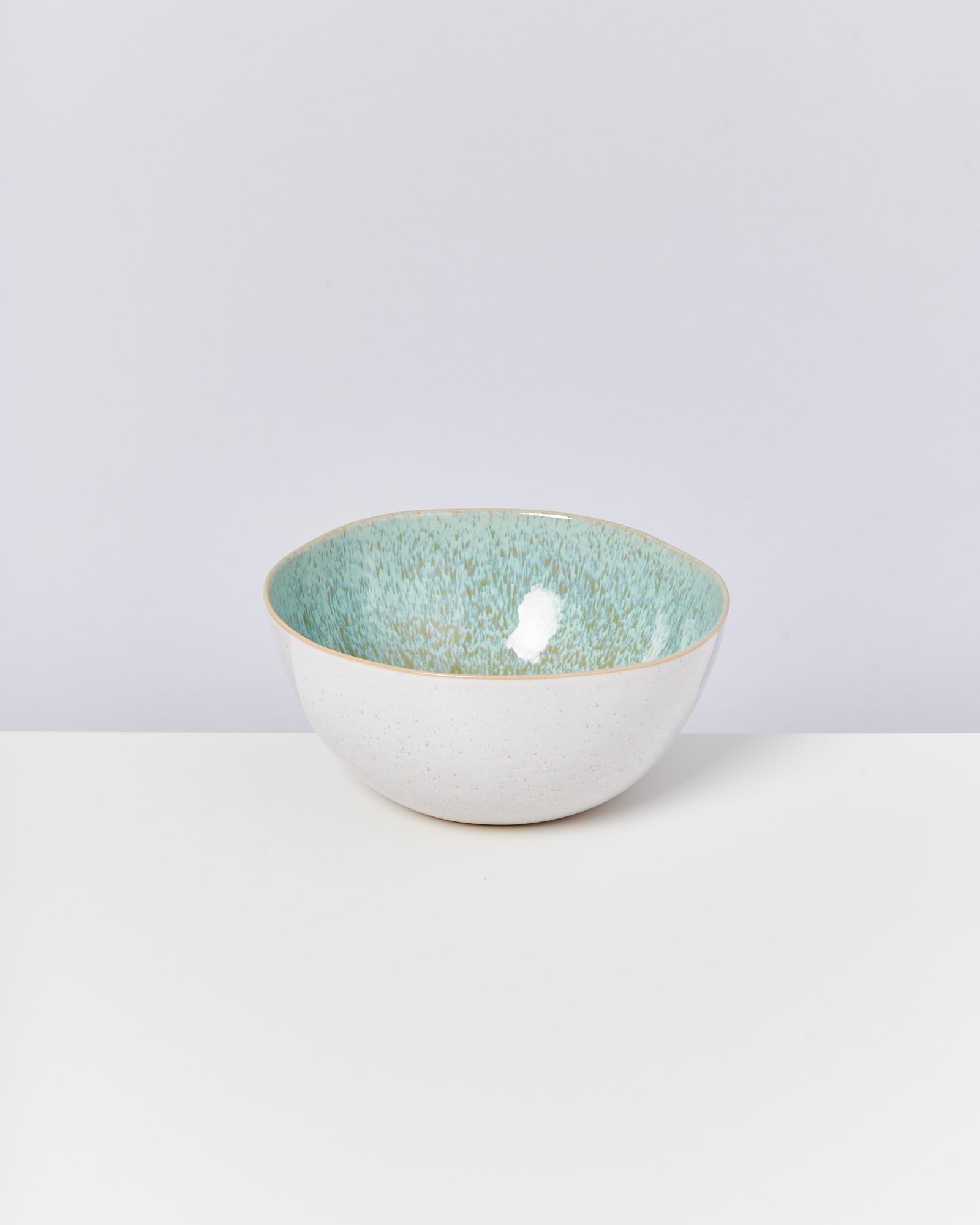 Keramikschüssel mit türkisfarbener Innenseite und weißer Außenseite steht auf einem weißen Tisch vor hellem Hintergrund.