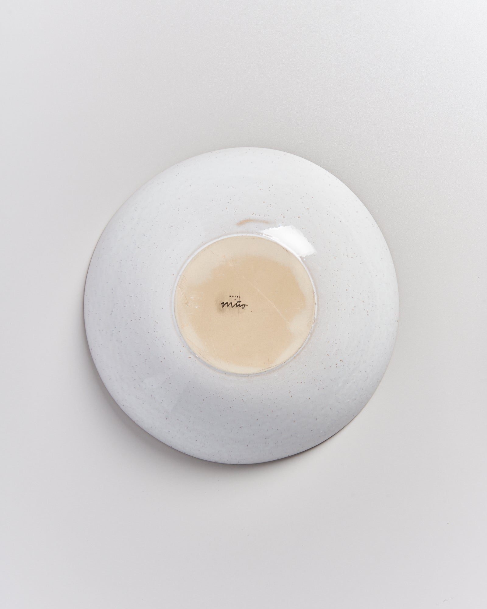 Ein umgedrehter, weißer Teller mit einem hellbraunen Zentrum und der Aufschrift "Mino".