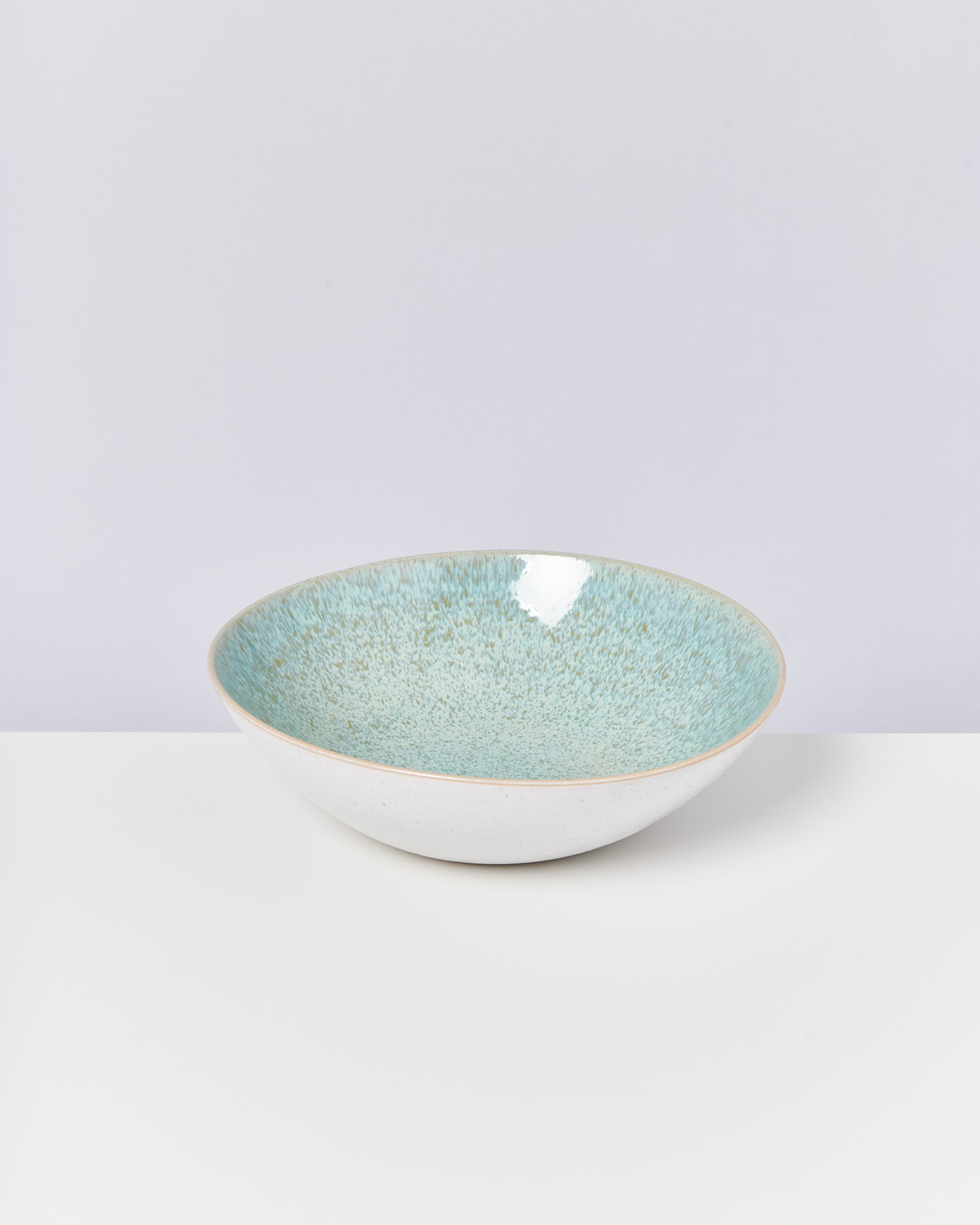 Ein tiefer, weißer Keramikteller mit blauer und grüner Glasur steht auf einer weißen Oberfläche.