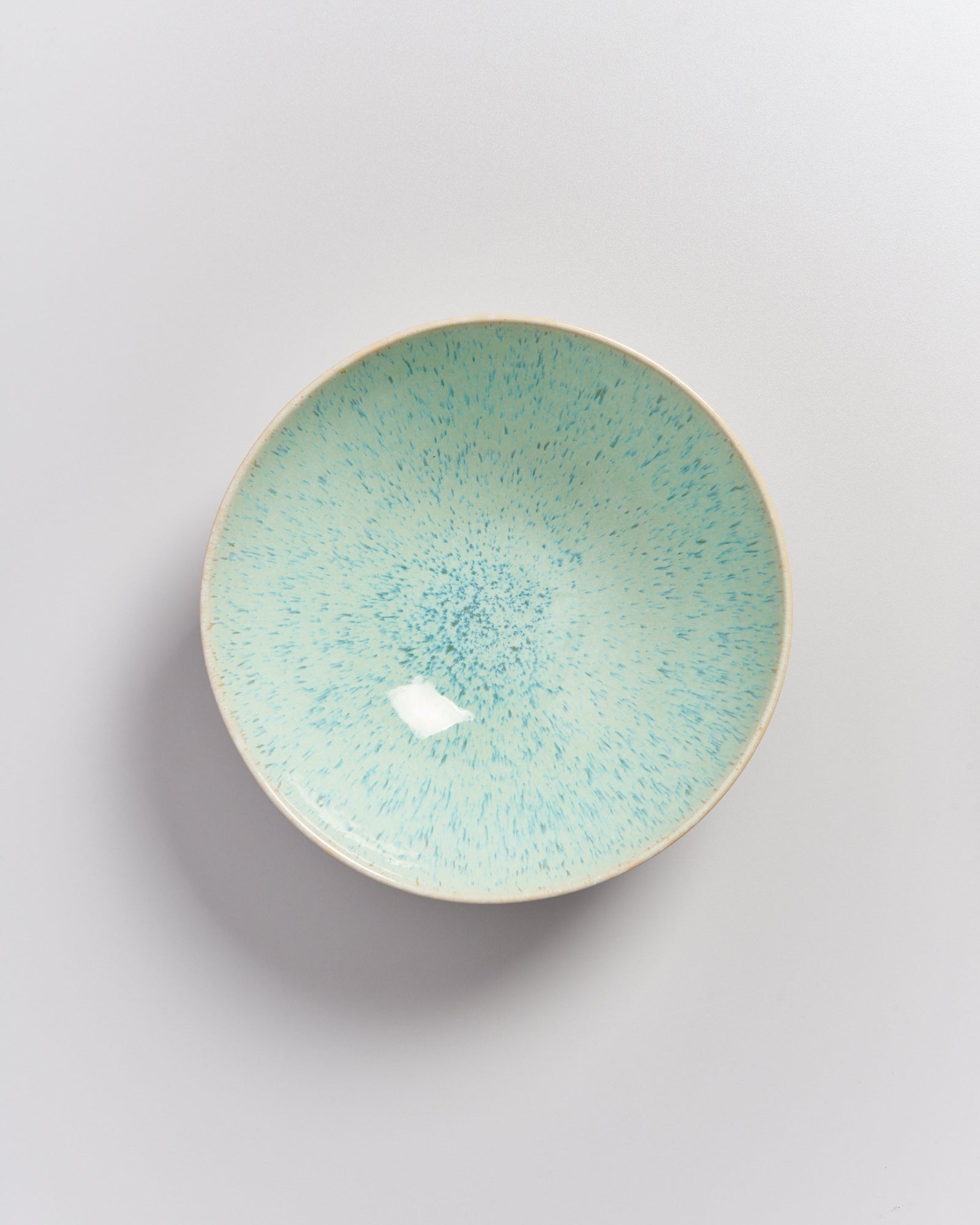 Türkis gesprenkelter Teller auf weißem Hintergrund.