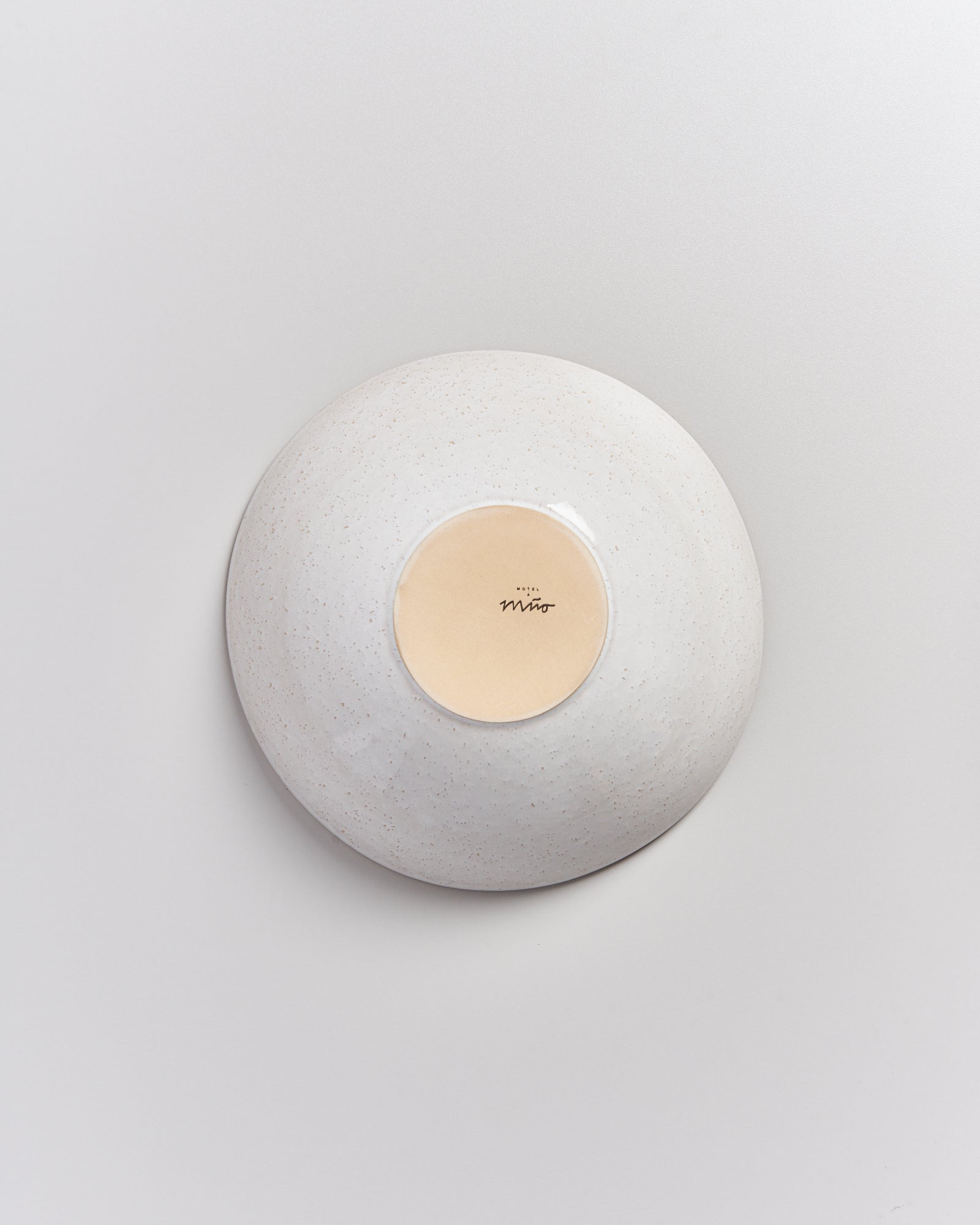 Eine umgedrehte, weiße Keramikschale mit einem Logo auf der Unterseite auf hellem Hintergrund.