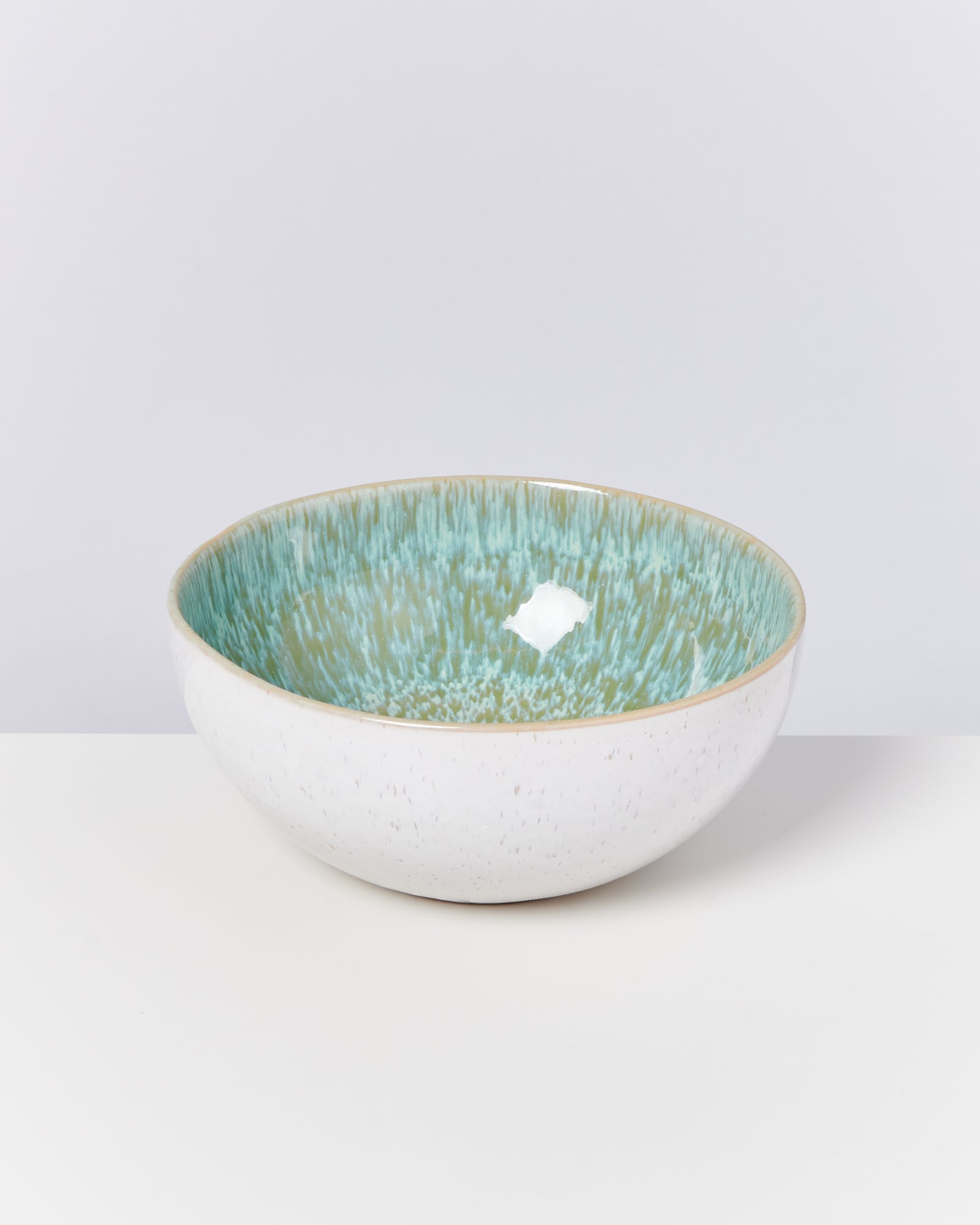 Weiße Schale mit grün-blauem Innendesign auf einem weißen Hintergrund.