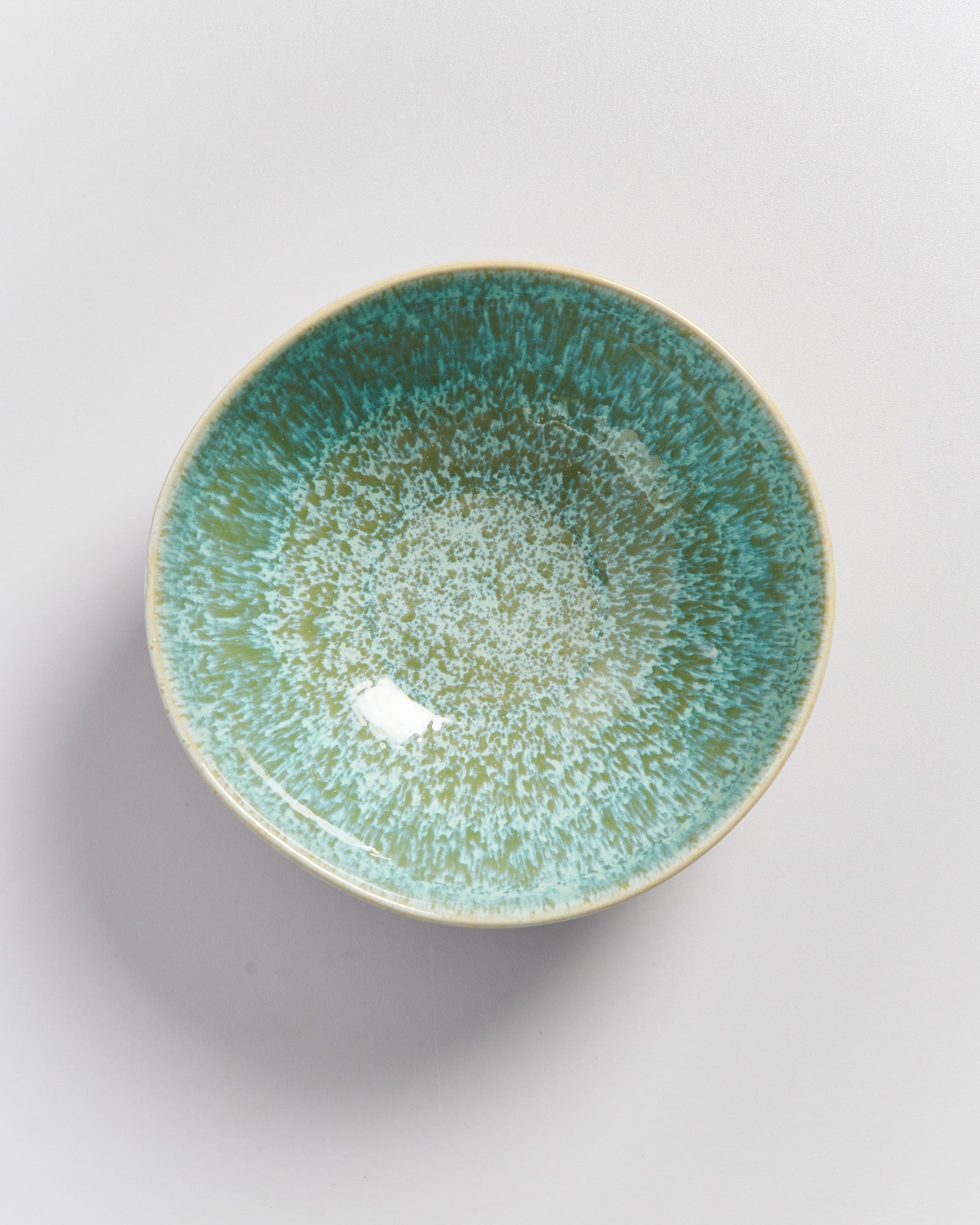Keramikschale mit grün-blauer, gesprenkelter Glasur auf hellem Hintergrund.