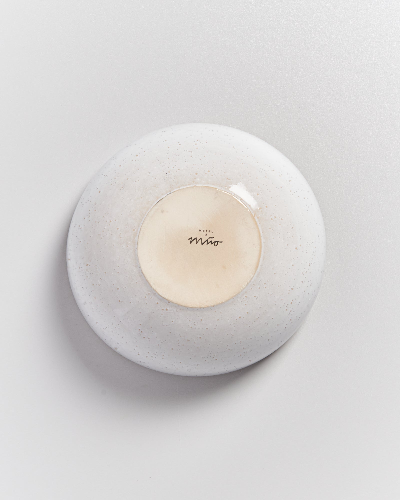 Rückseite einer weißen, gesprenkelten Keramikschale mit einer Aufschrift in der Mitte auf hellem Hintergrund.