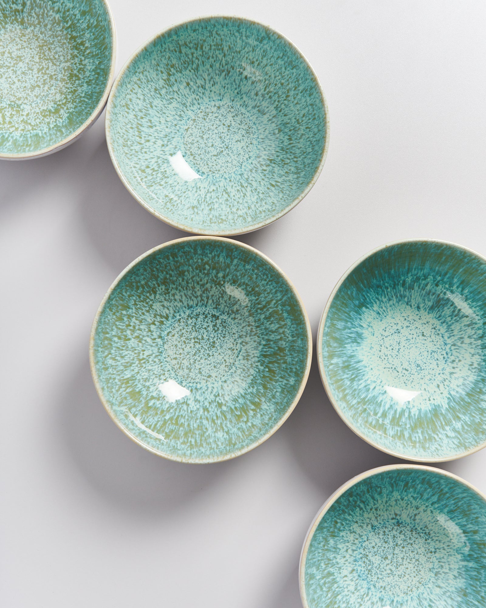 Fünf Keramikschalen mit grün-blauem Sprenkelmuster auf einer weißen Oberfläche angeordnet.