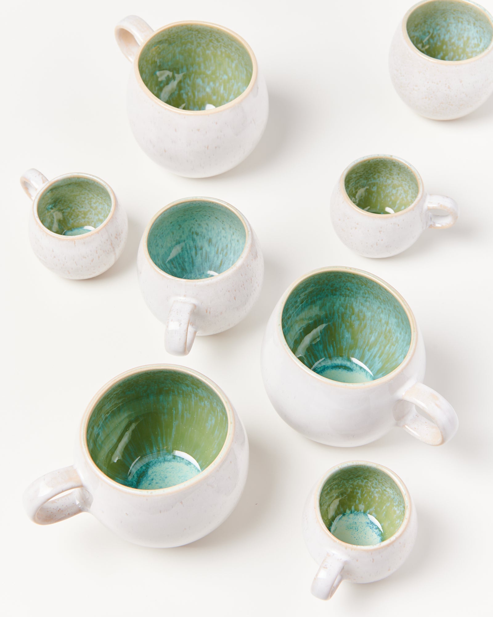 Keramiktassen mit grünem Inneren und cremefarbenem Äußeren sind auf einem weißen Hintergrund angeordnet.