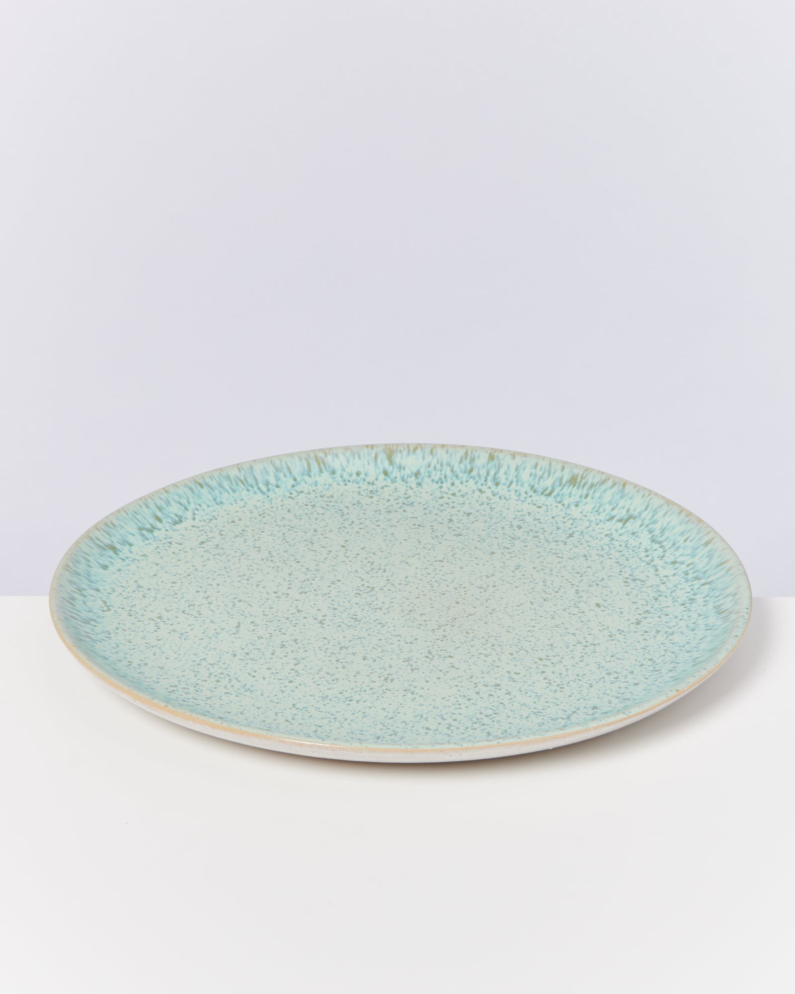 Ein türkisfarbener Teller mit gesprenkeltem Muster auf einer weißen Oberfläche.