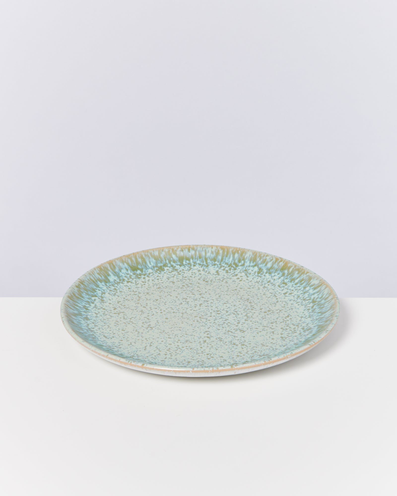 Ein runder, hellblauer Keramikteller mit gesprenkeltem Muster auf einem weißen Hintergrund.