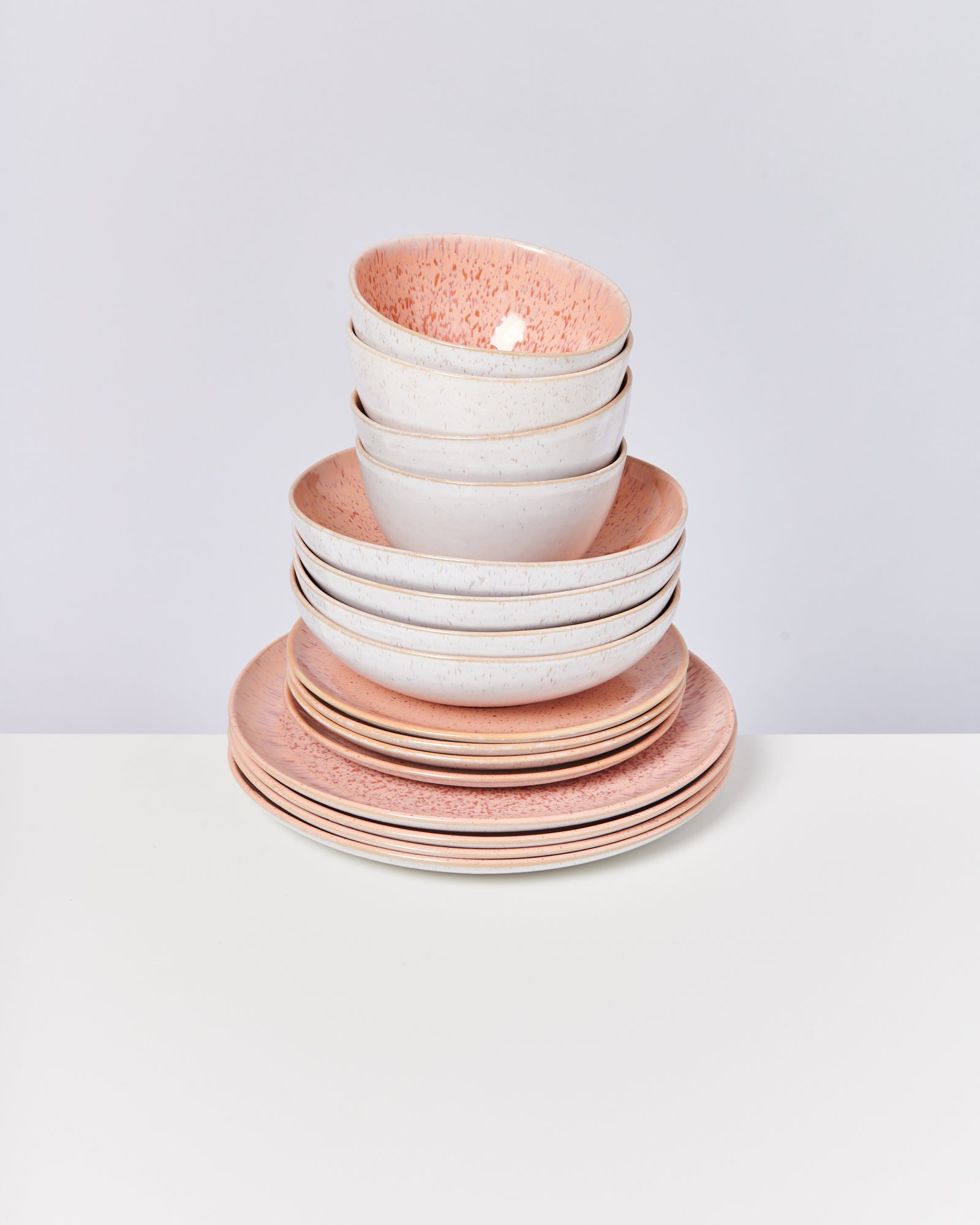 Ein Stapel aus weißen und rosafarbenen Keramiktellern und Schalen auf einem weißen Tisch.