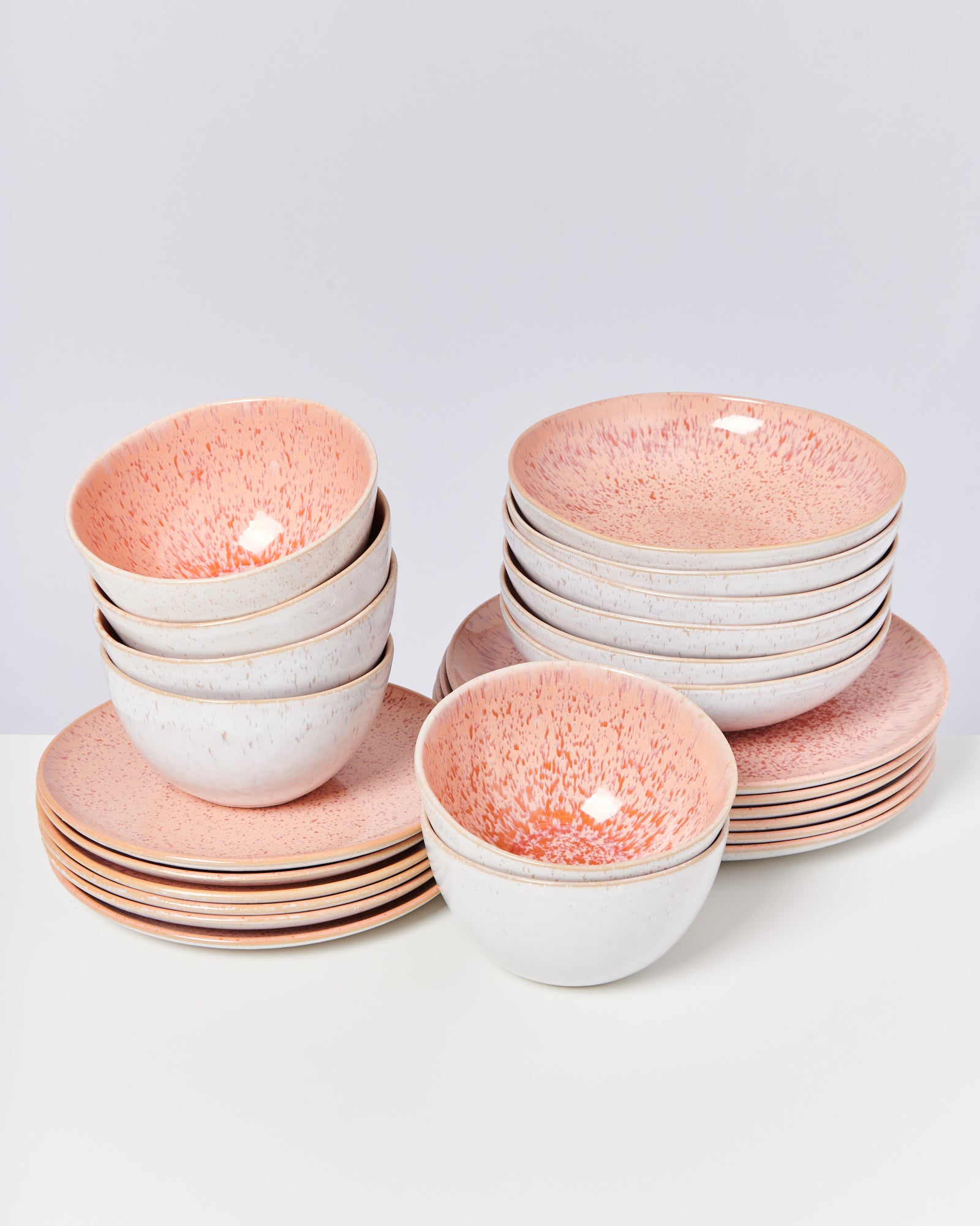 Stapel von Schalen und Tellern mit rosa Sprenkeln auf einem weißen Hintergrund.