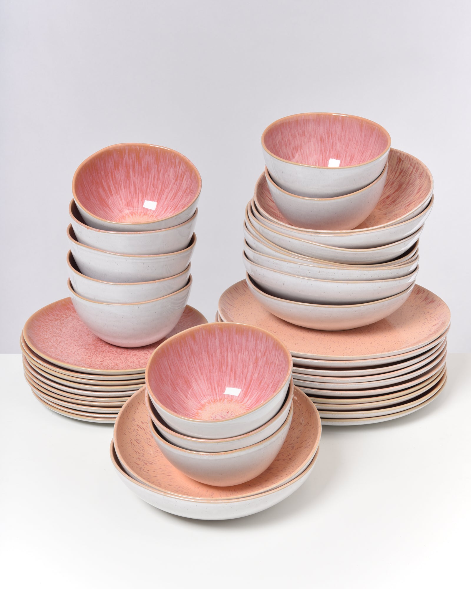 Mehrere gestapelte Schüsseln und Teller aus Keramik mit rosa Innenfläche vor weißem Hintergrund.