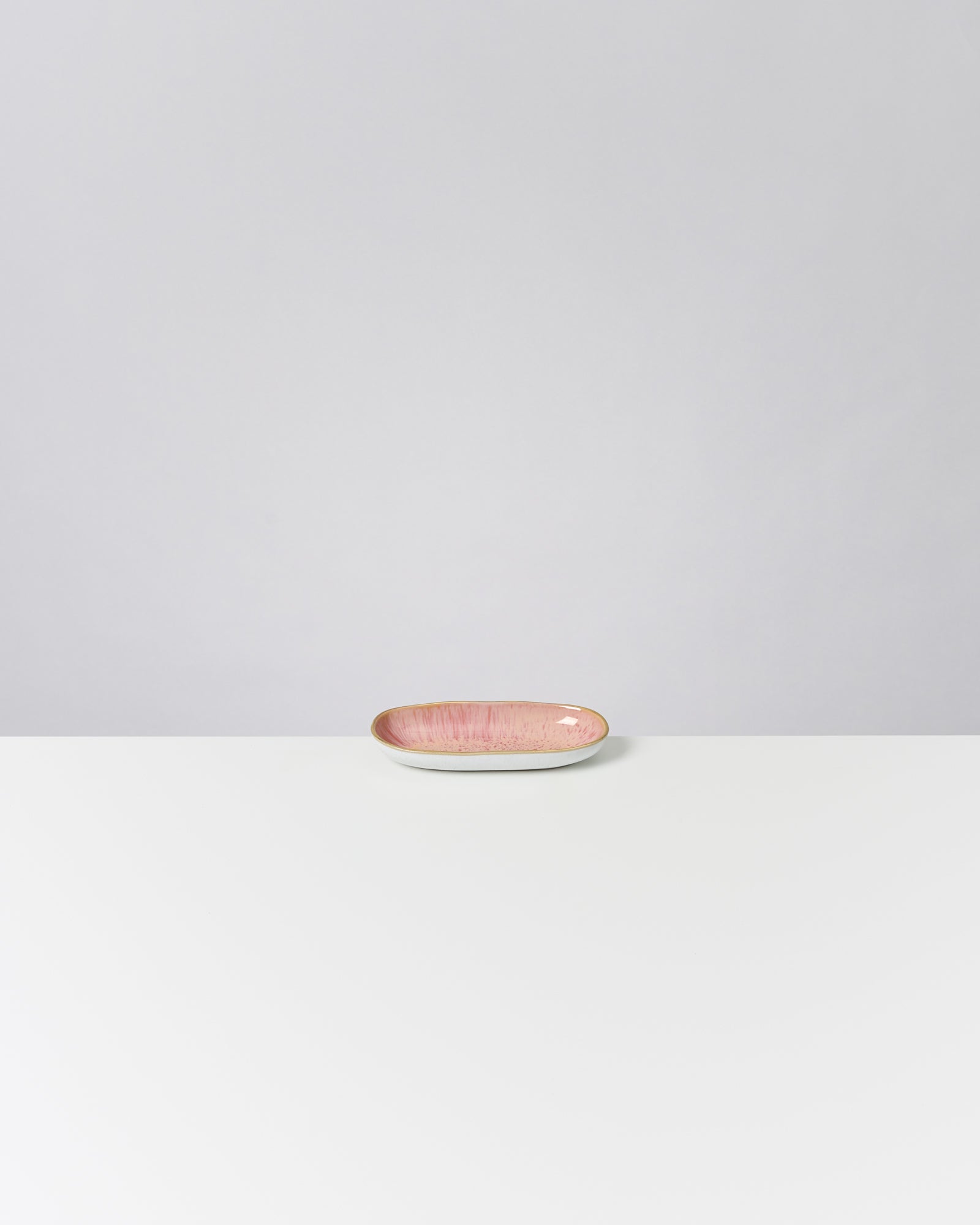 Rosa ovale Schale auf einem weißen Tisch vor grauem Hintergrund.