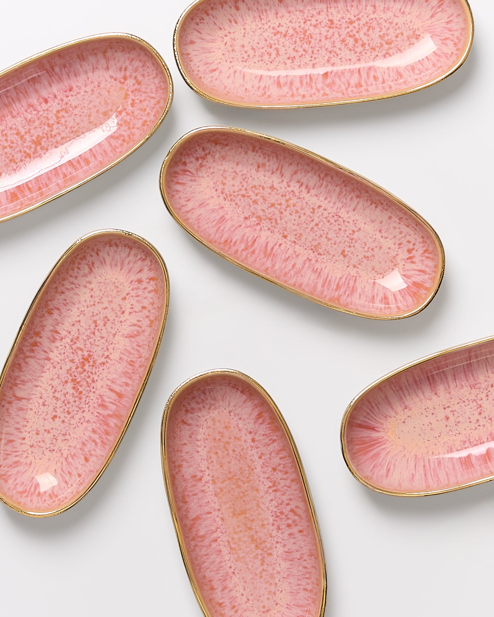 Sechs ovale, rosa Keramikteller mit goldenen Rändern auf weißem Hintergrund.