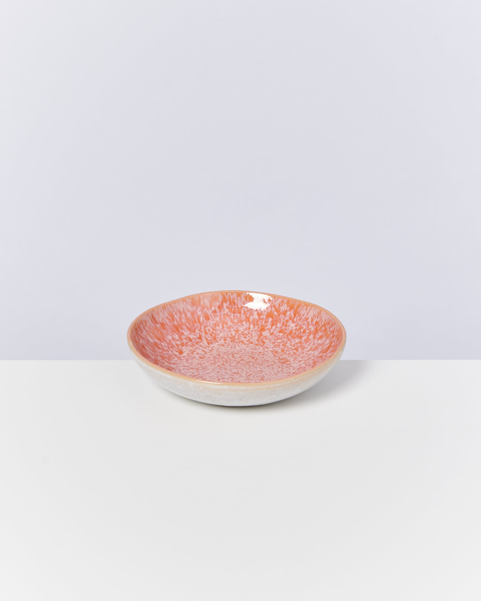 Orangefarbene Keramikschale mit gesprenkeltem Muster auf weißem Hintergrund.