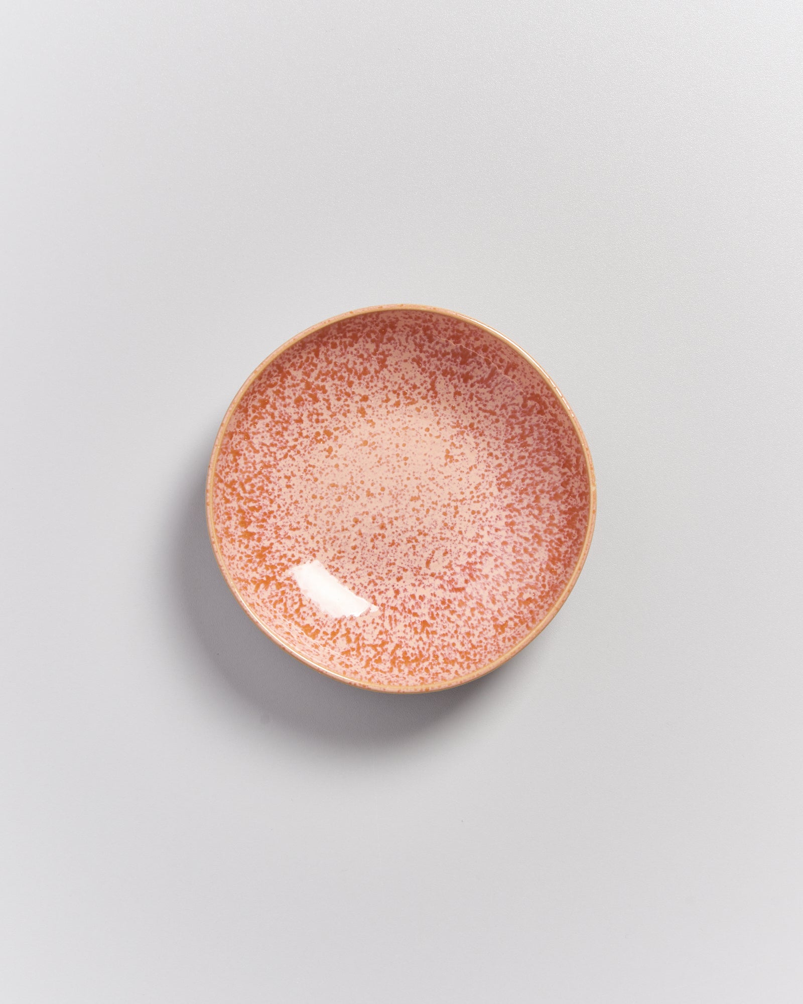 Ein rosafarben-gesprenkelter Keramikteller auf einem hellgrauen Hintergrund.